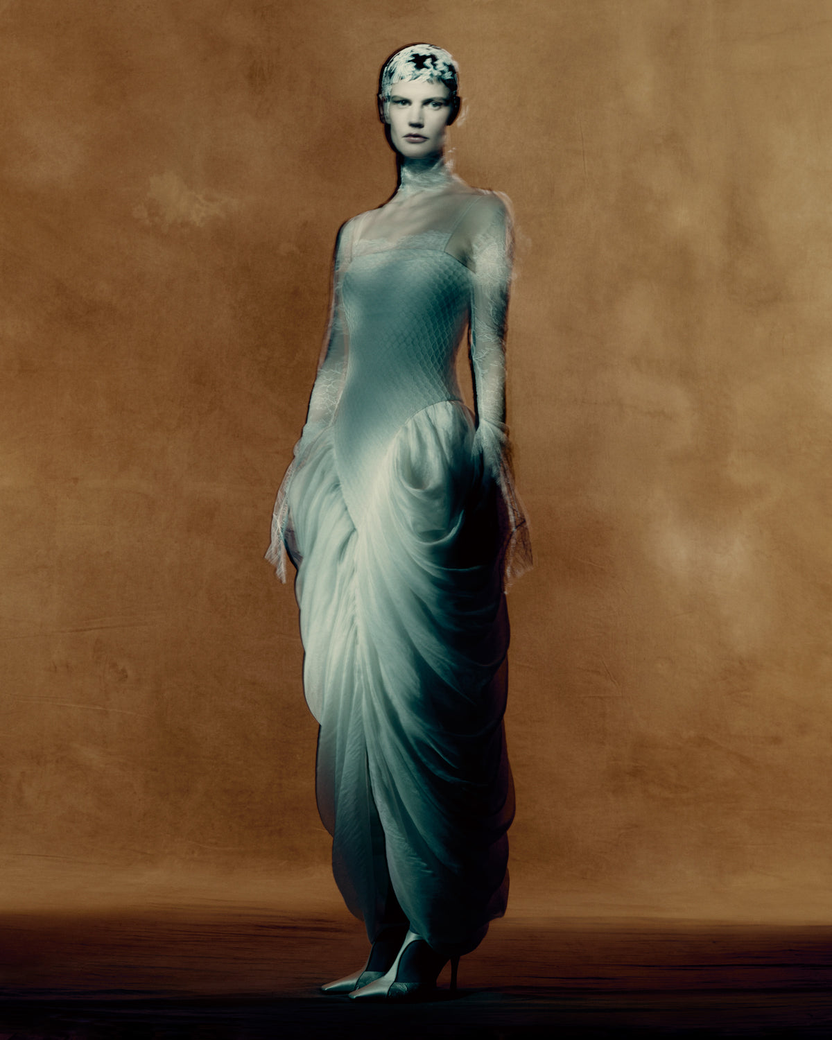 Spaghetti strap gown with a honeycomb lace layered over a silk and wool gauze elongated bodice, with delicate chantilly lace peeking from behind the neckline. Cascading draping falls from the waist creating a tulip skirt silhouette. Internal grosgrain waist belt, invisible zip at center back. 