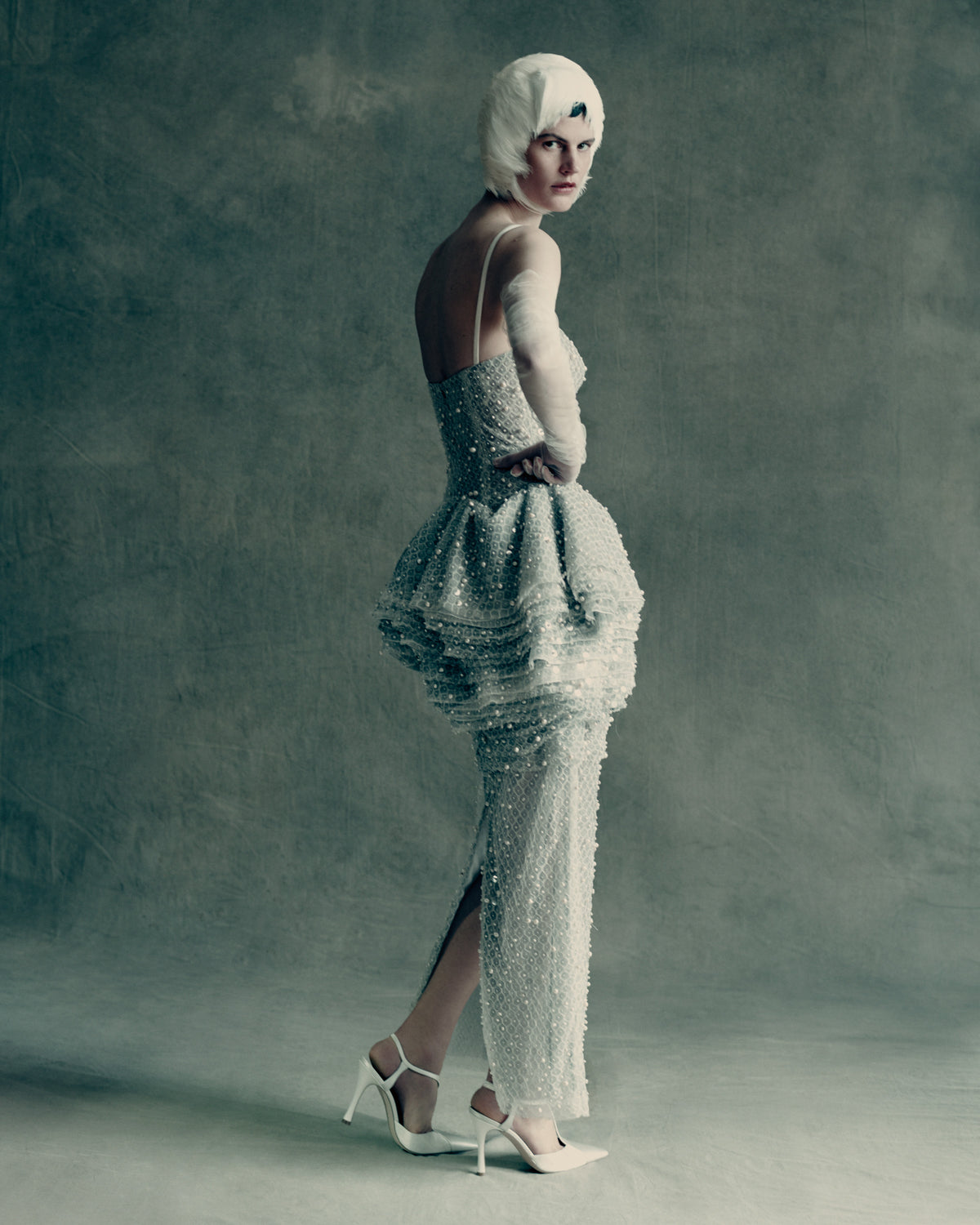 Pegged column gown with tiered peplum skirt and delicate spaghetti straps. Cascading layers of soft tulle, silk organza, and honeycomb lace are delicately hand-embroidered with genuine baroque pearls and transparent sequins. Soft internal bobbinete bustier, grosgrain waistbelt, and invisible zip closure at center back. 