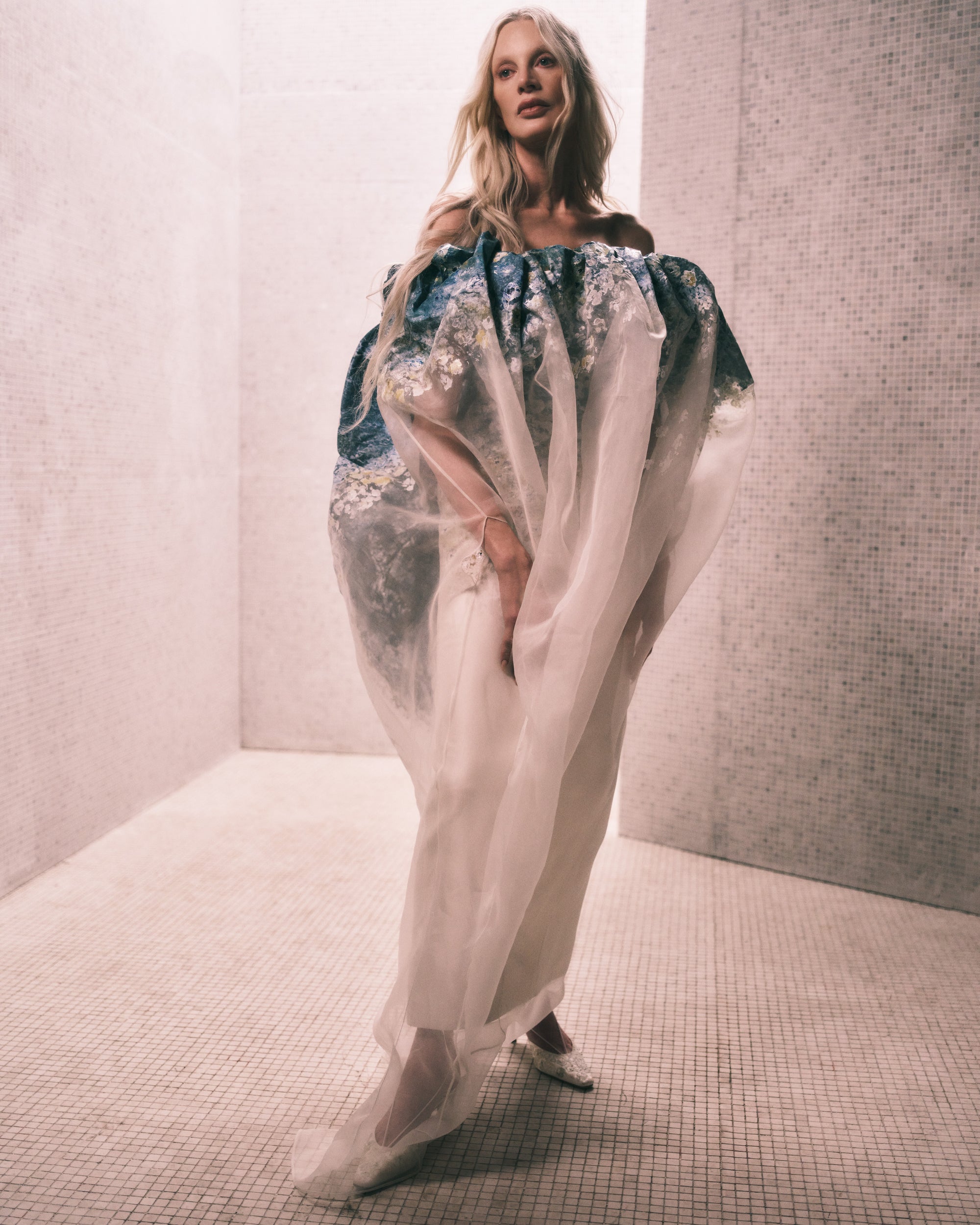 Floral degrade hand painted silk wool twill column gown with exaggerated flared neckline layered with hand painted transparent silk organza tapered bubbled overlay. Boned internal bustier, internal grosgrain belt and invisible zip closure at center back.