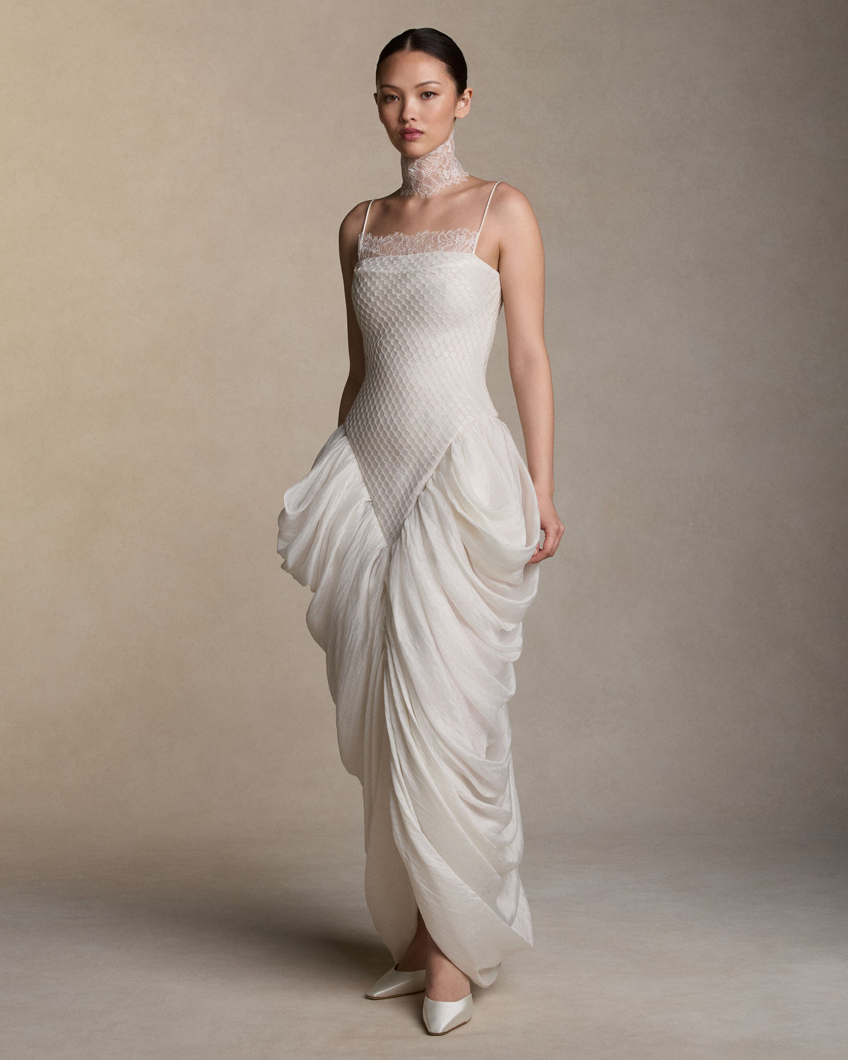 Spaghetti strap gown with a honeycomb lace layered over a silk and wool gauze elongated bodice, with delicate chantilly lace peeking from behind the neckline. Cascading draping falls from the waist creating a tulip skirt silhouette. Internal grosgrain waist belt, invisible zip at center back. 