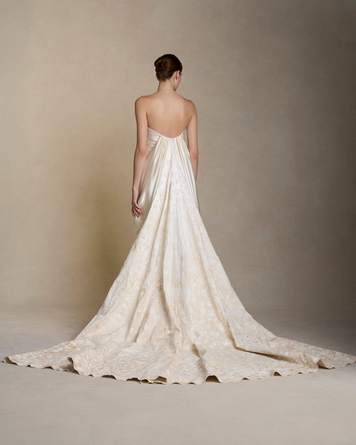 Floral hand painted silk wool twill strapless column gown. Fluid silk wool drape falls from center front and wraps the hip transcending into a watteau at center back. Removable train is scattered with hand painted florals throughout. Boned internal bustier, internal grosgrain belt and invisible zip closure at center back.