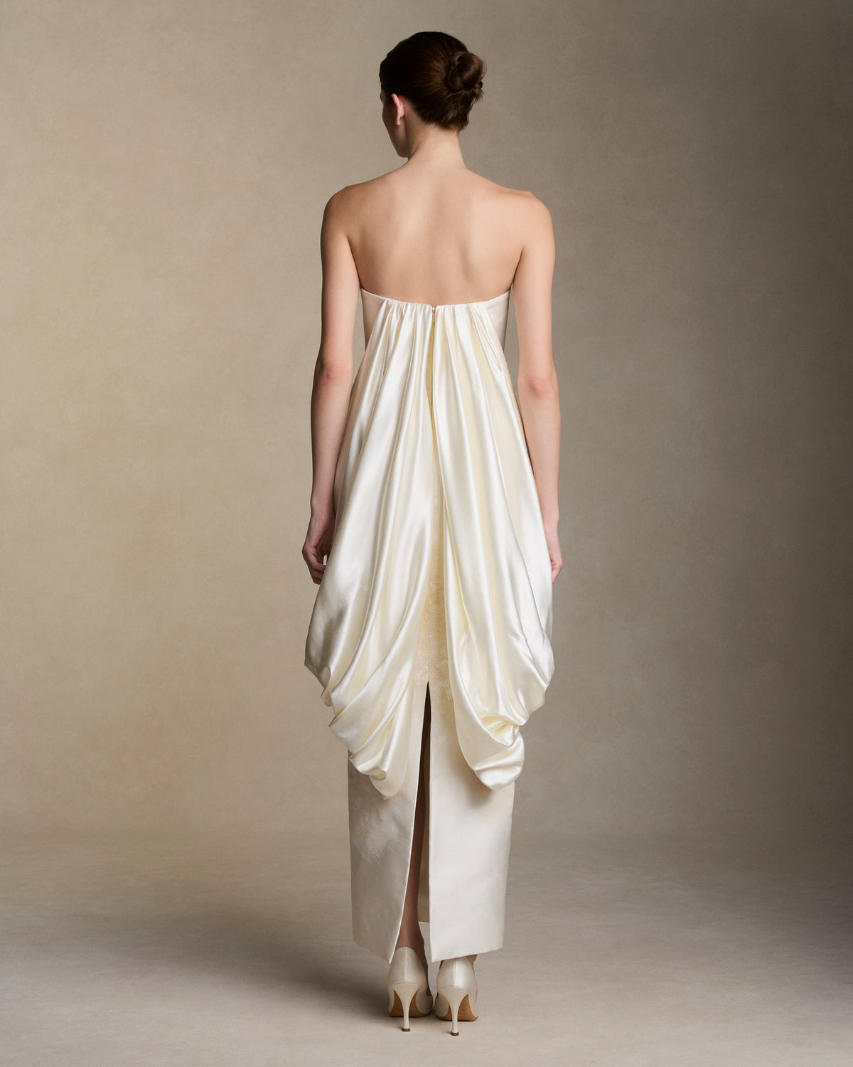 Floral hand painted silk wool twill strapless column gown. Fluid silk wool drape falls from center front and wraps the hip transcending into a watteau at center back. Removable train is scattered with hand painted florals throughout. Boned internal bustier, internal grosgrain belt and invisible zip closure at center back.