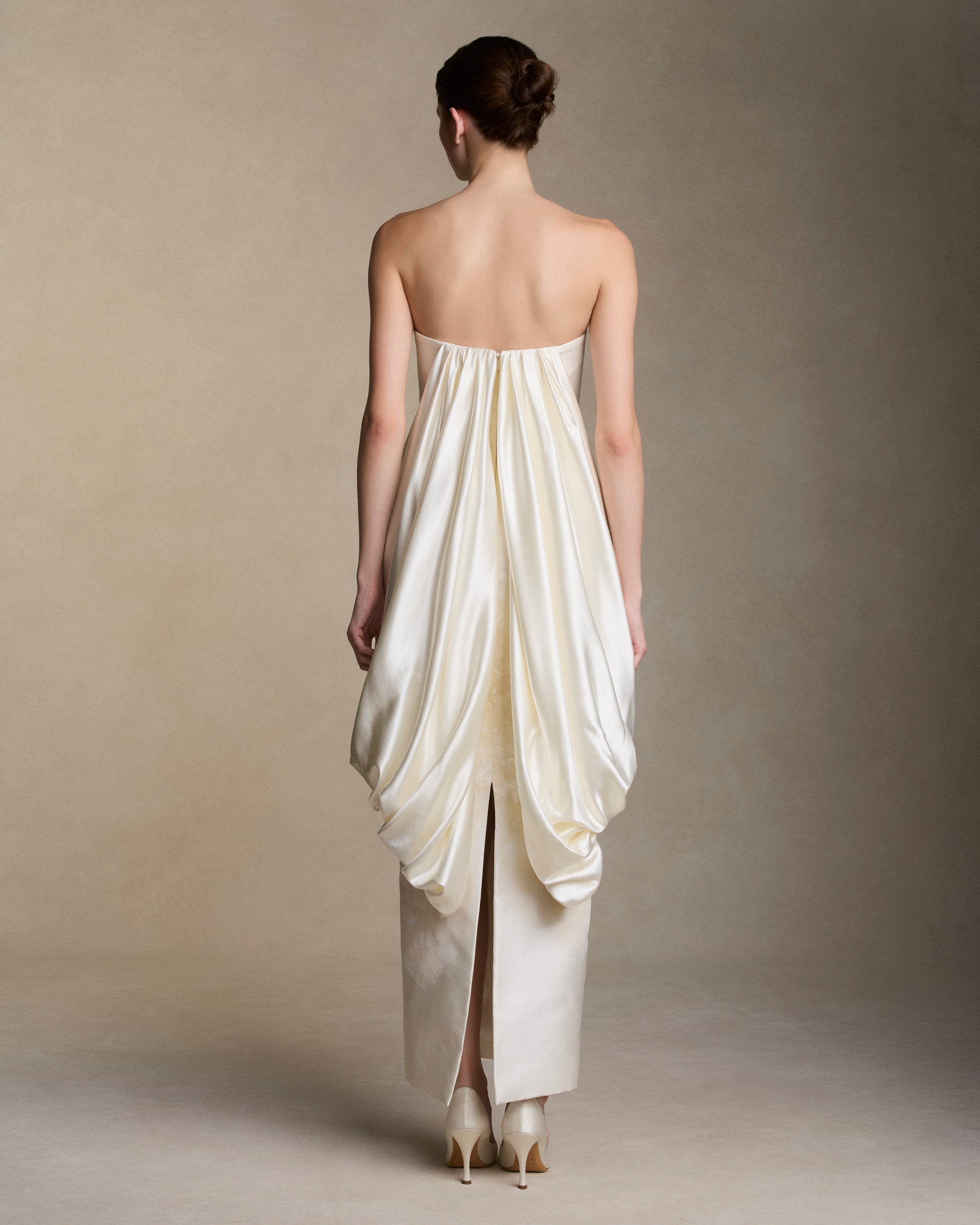 Floral hand painted silk wool twill strapless column gown. Fluid silk wool drape falls from center front and wraps the hip transcending into a watteau at center back. Removable train is scattered with hand painted florals throughout. Boned internal bustier, internal grosgrain belt and invisible zip closure at center back.