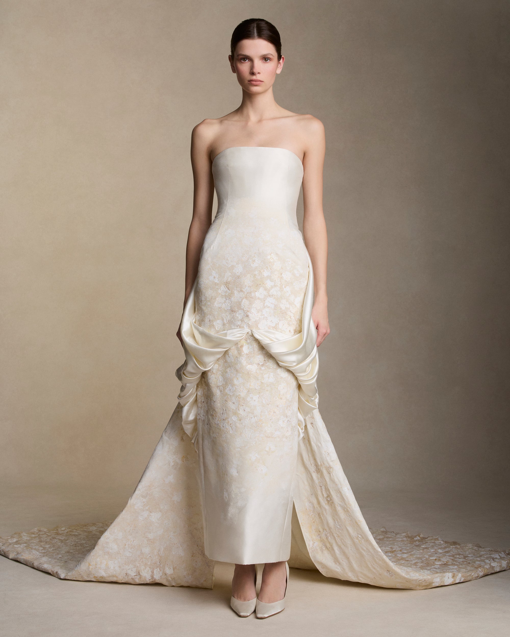 Floral hand painted silk wool twill strapless column gown. Fluid silk wool drape falls from center front and wraps the hip transcending into a watteau at center back. Removable train is scattered with hand painted florals throughout. Boned internal bustier, internal grosgrain belt and invisible zip closure at center back.