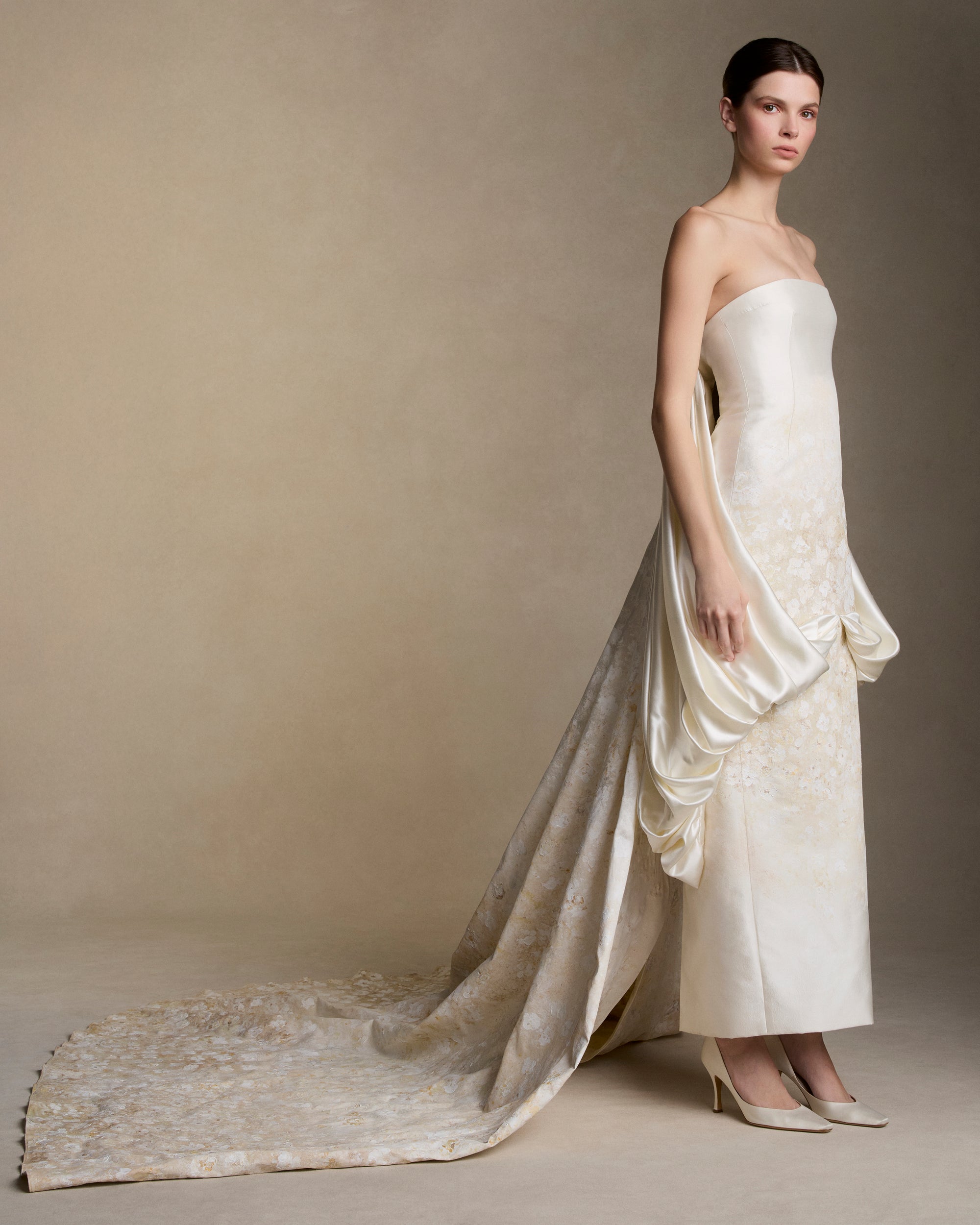 Floral hand painted silk wool twill strapless column gown. Fluid silk wool drape falls from center front and wraps the hip transcending into a watteau at center back. Removable train is scattered with hand painted florals throughout. Boned internal bustier, internal grosgrain belt and invisible zip closure at center back.