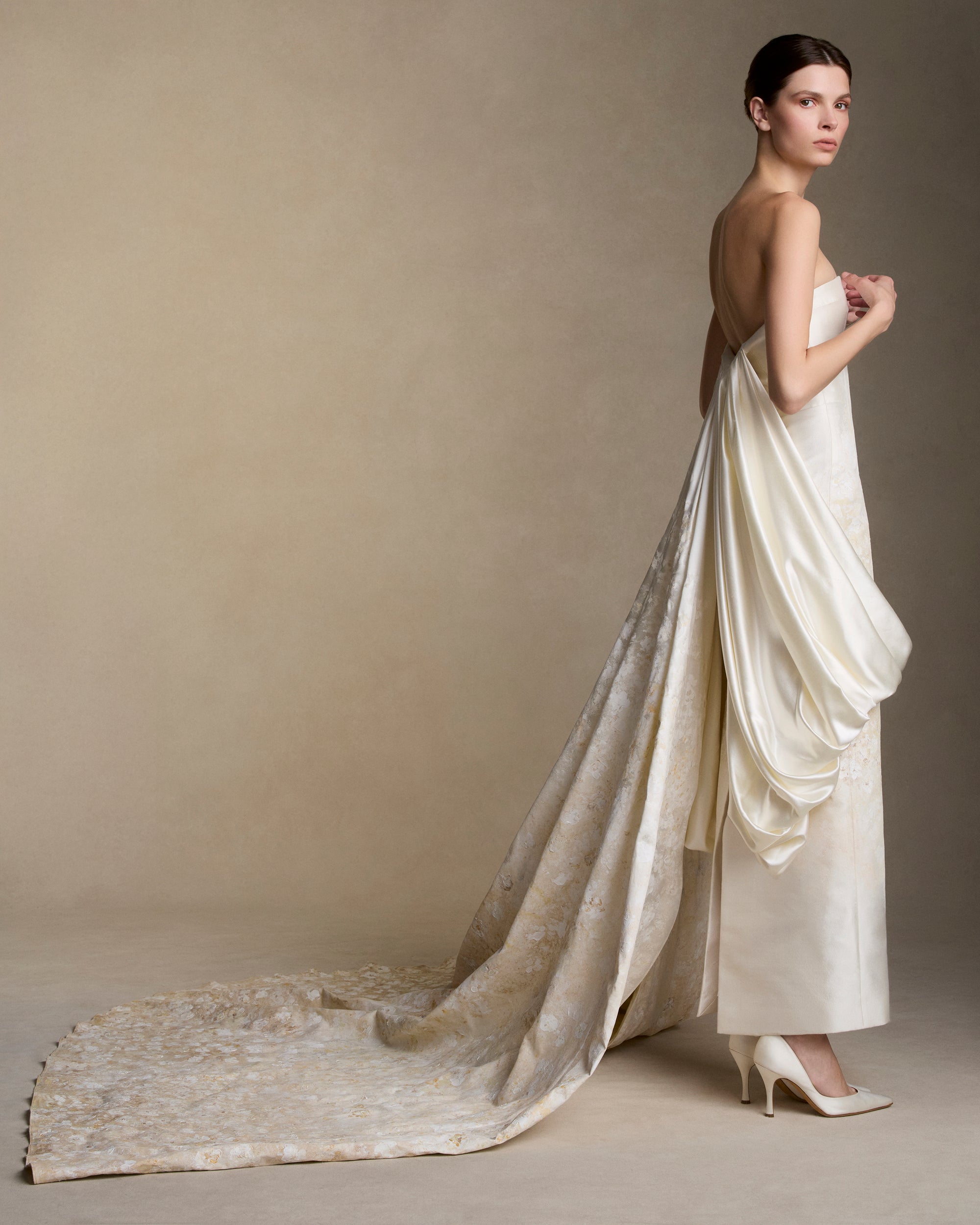 Floral hand painted silk wool twill strapless column gown. Fluid silk wool drape falls from center front and wraps the hip transcending into a watteau at center back. Removable train is scattered with hand painted florals throughout. Boned internal bustier, internal grosgrain belt and invisible zip closure at center back.