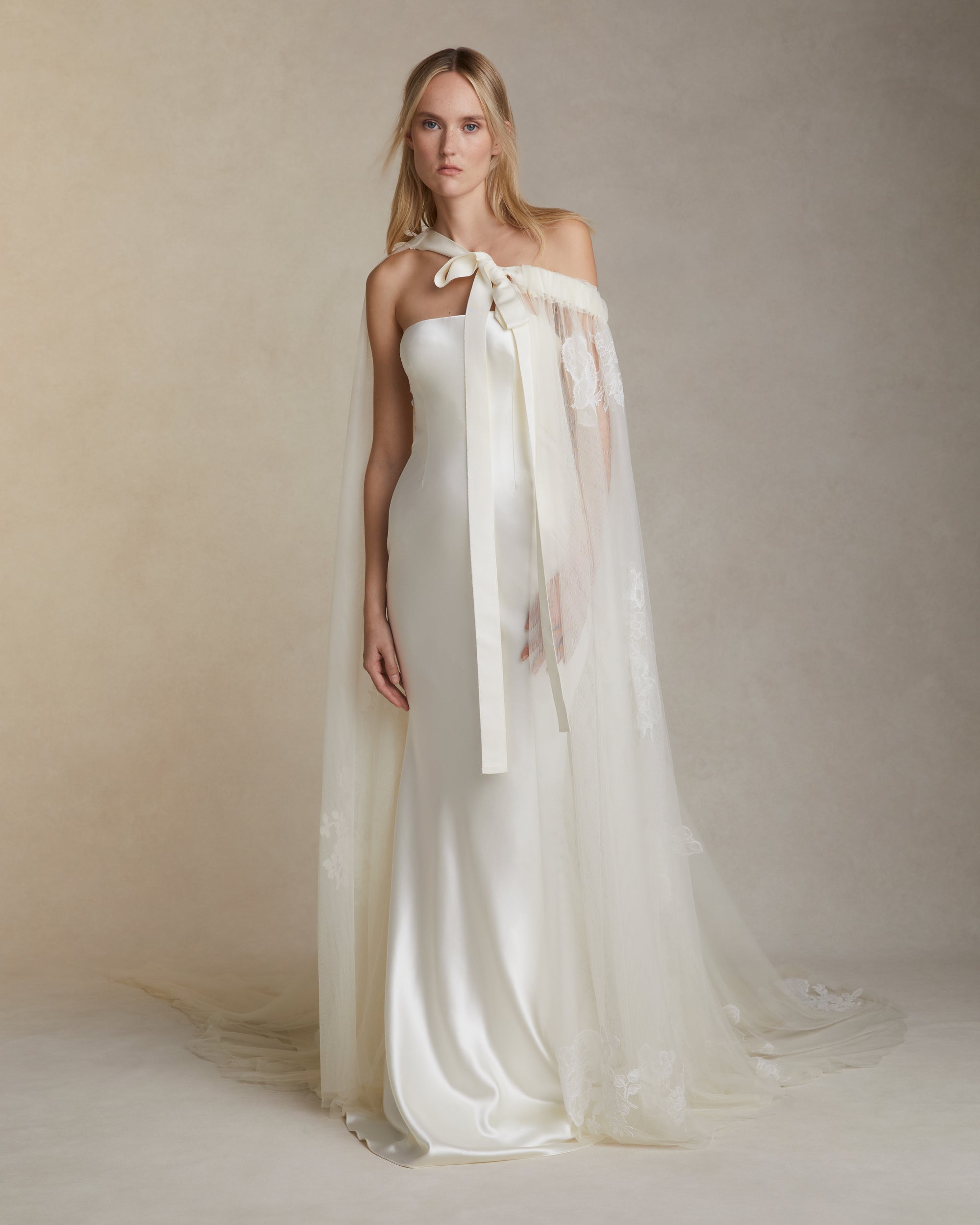 Soft tulle cape decorated with hand cut Chantilly and corded lace appliqués throughout Undulating hem measures 85” at longest point. Grosgrain ribbon tie.