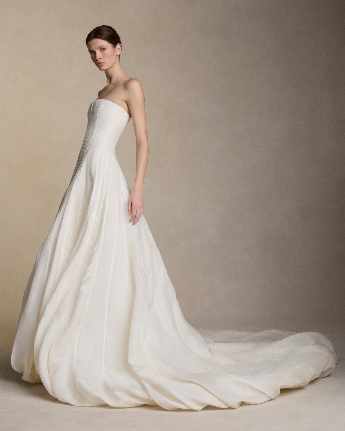 Strapless silk linen organza ballgown with dramatic train. Rows of grosgrain boning detail shape the bodice and disperse into undulating panels, finishing with a bubble hem. Boned internal bustier, internal grosgrain belt and invisible zip closure at center back.