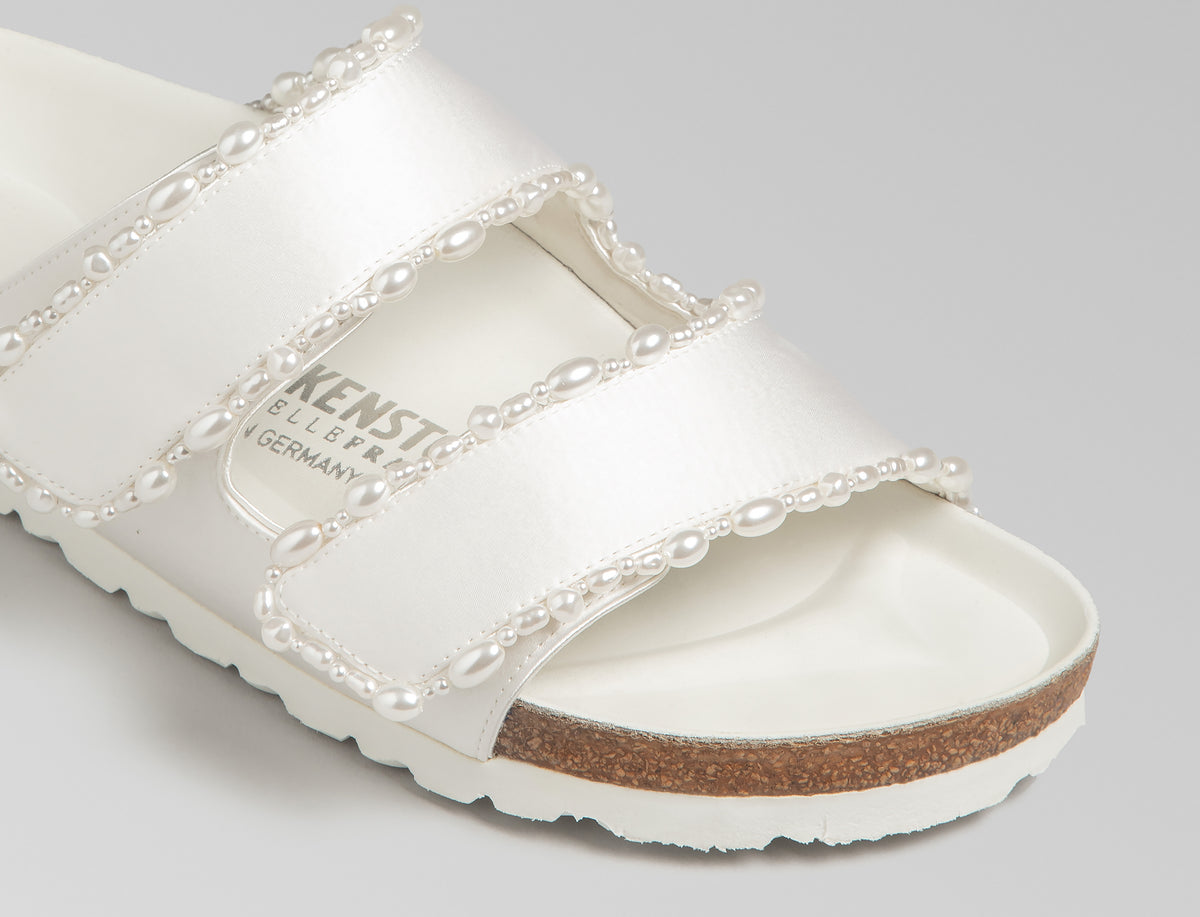 The Arizona is elevated in luminous ivory satin with piped trim detail, accented with delicate pearl edging for a refined and ceremonial finish. The design also introduces an innovative adjustable hidden buckle closure. Handcrafted in Germany, the shoe blends BIRKENSTOCK’s iconic comfort with Danielle Frankel’s bridal elegance.- Upper: Delicate satin upper material- Footbed: Anatomical shaped BIRKENSTOCK cork latex Footbed lined with premium Nappa Leather- Sole: EVA die cut outsole with a custom design, blending classic BIRKENSTOCK bone pattern with delicate lace inspired detailing
