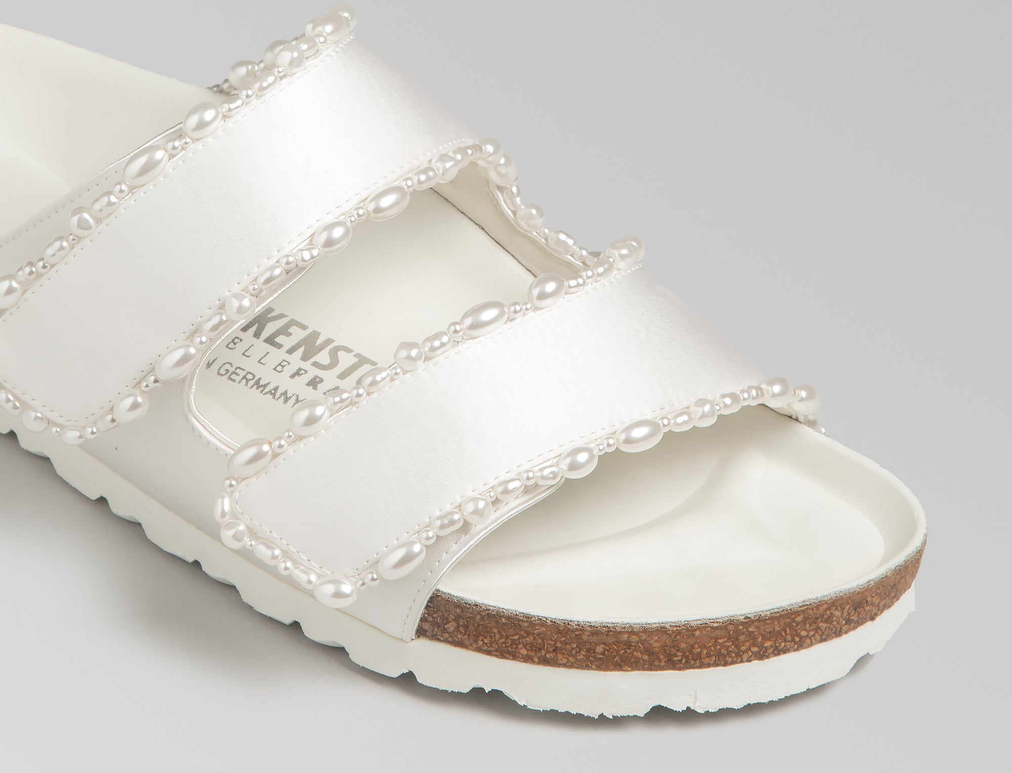 The Arizona is elevated in luminous ivory satin with piped trim detail, accented with delicate pearl edging for a refined and ceremonial finish. The design also introduces an innovative adjustable hidden buckle closure. Handcrafted in Germany, the shoe blends BIRKENSTOCK’s iconic comfort with Danielle Frankel’s bridal elegance.- Upper: Delicate satin upper material- Footbed: Anatomical shaped BIRKENSTOCK cork latex Footbed lined with premium Nappa Leather- Sole: EVA die cut outsole with a custom design, blending classic BIRKENSTOCK bone pattern with delicate lace inspired detailing