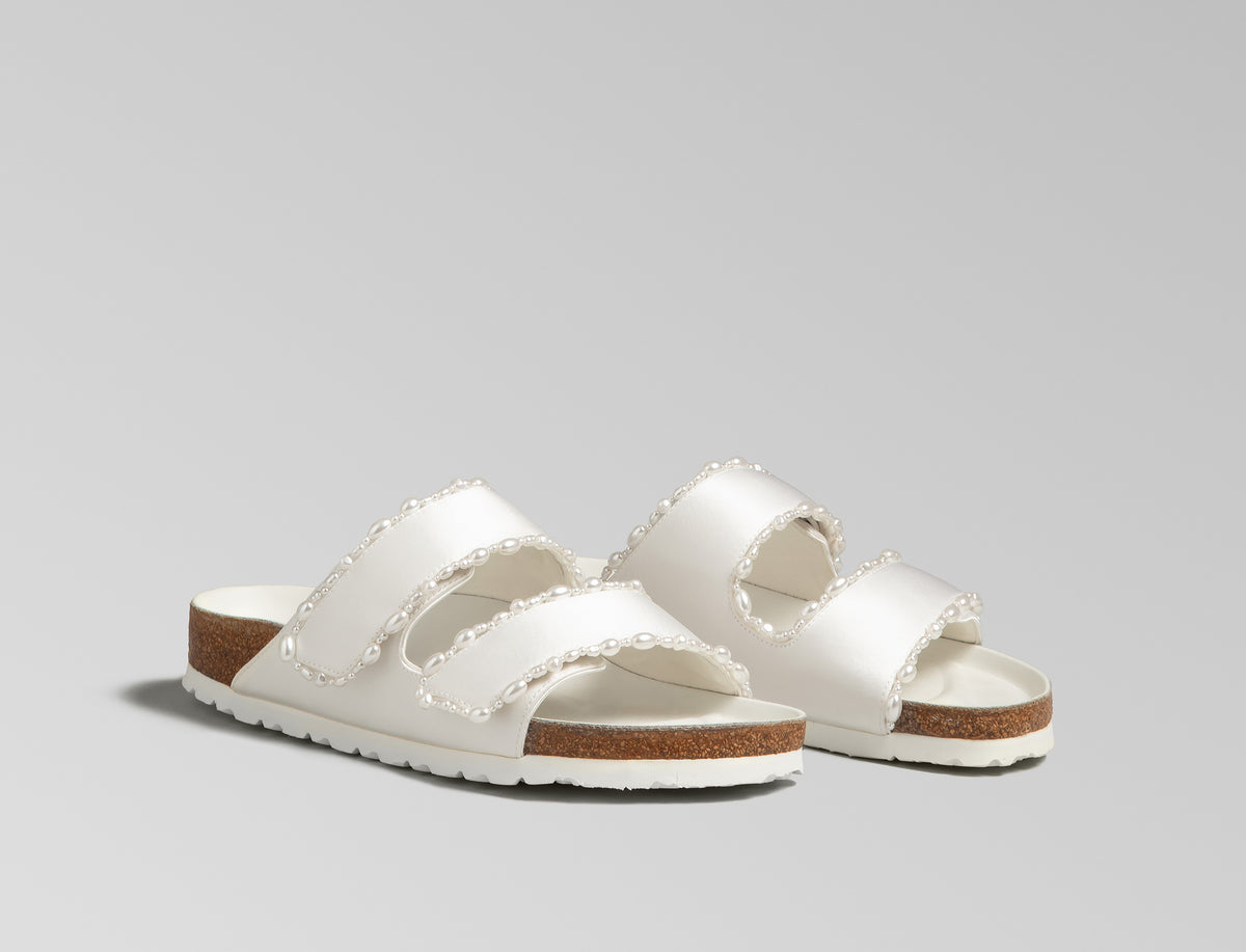The Arizona is elevated in luminous ivory satin with piped trim detail, accented with delicate pearl edging for a refined and ceremonial finish. The design also introduces an innovative adjustable hidden buckle closure. Handcrafted in Germany, the shoe blends BIRKENSTOCK’s iconic comfort with Danielle Frankel’s bridal elegance.- Upper: Delicate satin upper material- Footbed: Anatomical shaped BIRKENSTOCK cork latex Footbed lined with premium Nappa Leather- Sole: EVA die cut outsole with a custom design, blending classic BIRKENSTOCK bone pattern with delicate lace inspired detailing