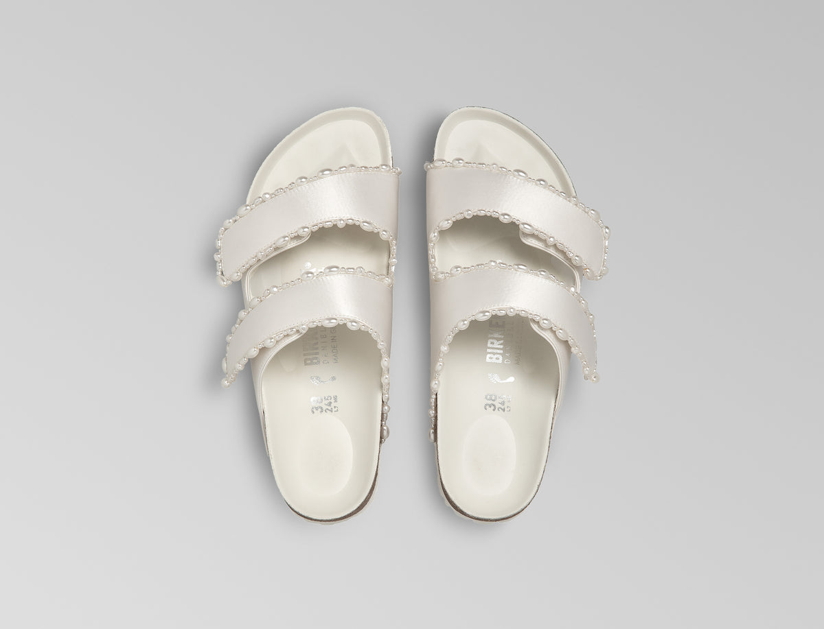 The Arizona is elevated in luminous ivory satin with piped trim detail, accented with delicate pearl edging for a refined and ceremonial finish. The design also introduces an innovative adjustable hidden buckle closure. Handcrafted in Germany, the shoe blends BIRKENSTOCK’s iconic comfort with Danielle Frankel’s bridal elegance.- Upper: Delicate satin upper material- Footbed: Anatomical shaped BIRKENSTOCK cork latex Footbed lined with premium Nappa Leather- Sole: EVA die cut outsole with a custom design, blending classic BIRKENSTOCK bone pattern with delicate lace inspired detailing