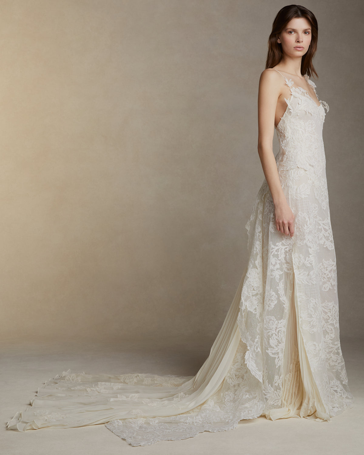 Lyon lace gown with pleated chiffon godets and hand cut Lyon lace applique throughout. Hand cut lace adorns the spaghetti straps and watteau peels from center back releasing into an extended pleated chiffon train. Soft internal bustier. Invisible zip closure at center back.