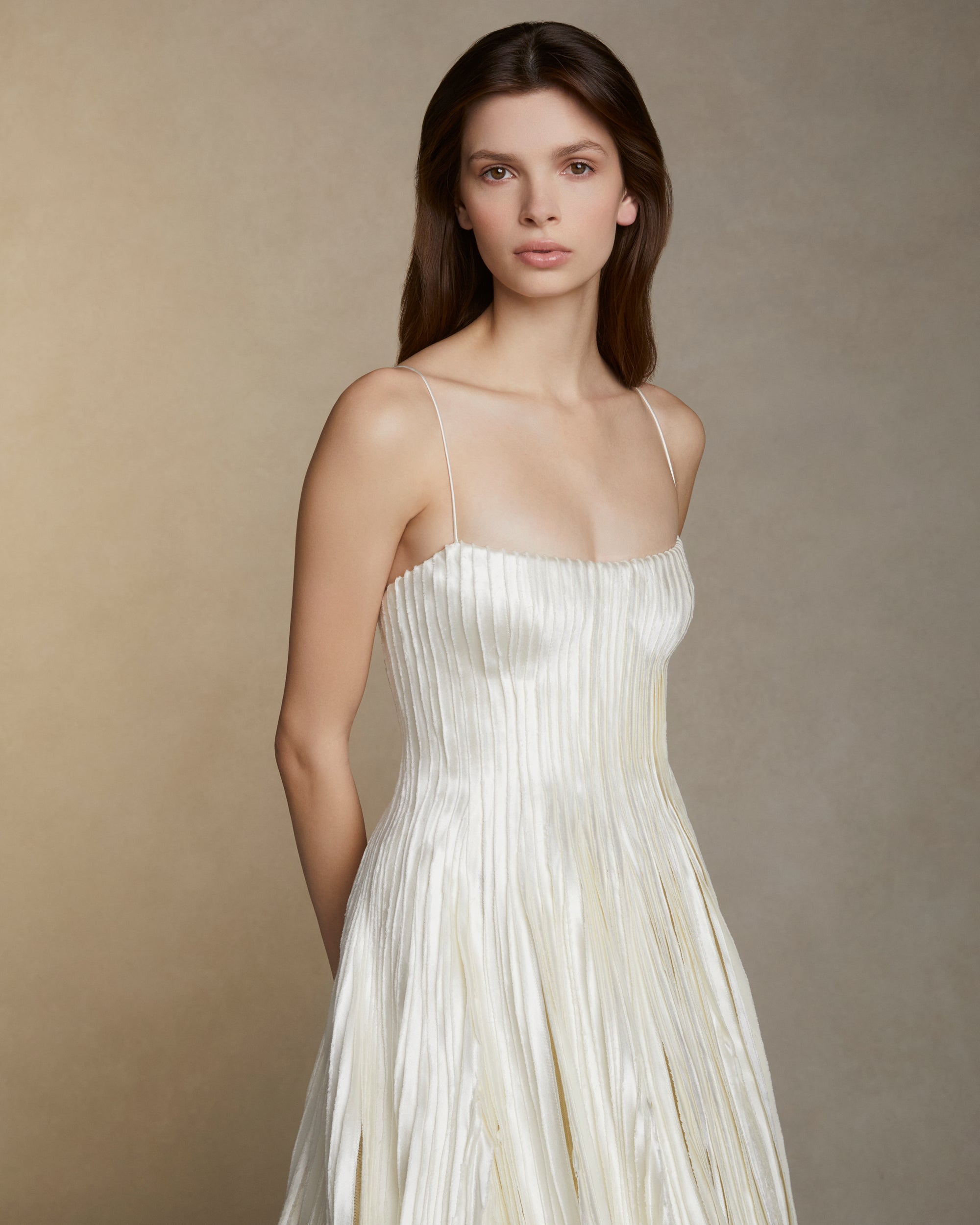 Soft scoop neck ballgown decorated with hand cut and hand frayed bias silk wool strip fabric technique embroidery. Layers of silk wool bias cascade organically into a bubble hem train. Internal bustier with invisible zip closure at center back.
