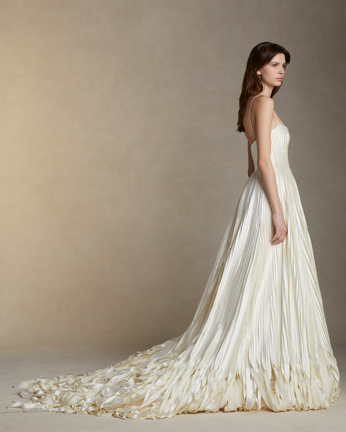Soft scoop neck ballgown decorated with hand cut and hand frayed bias silk wool strip fabric technique embroidery. Layers of silk wool bias cascade organically into a bubble hem train. Internal bustier with invisible zip closure at center back.