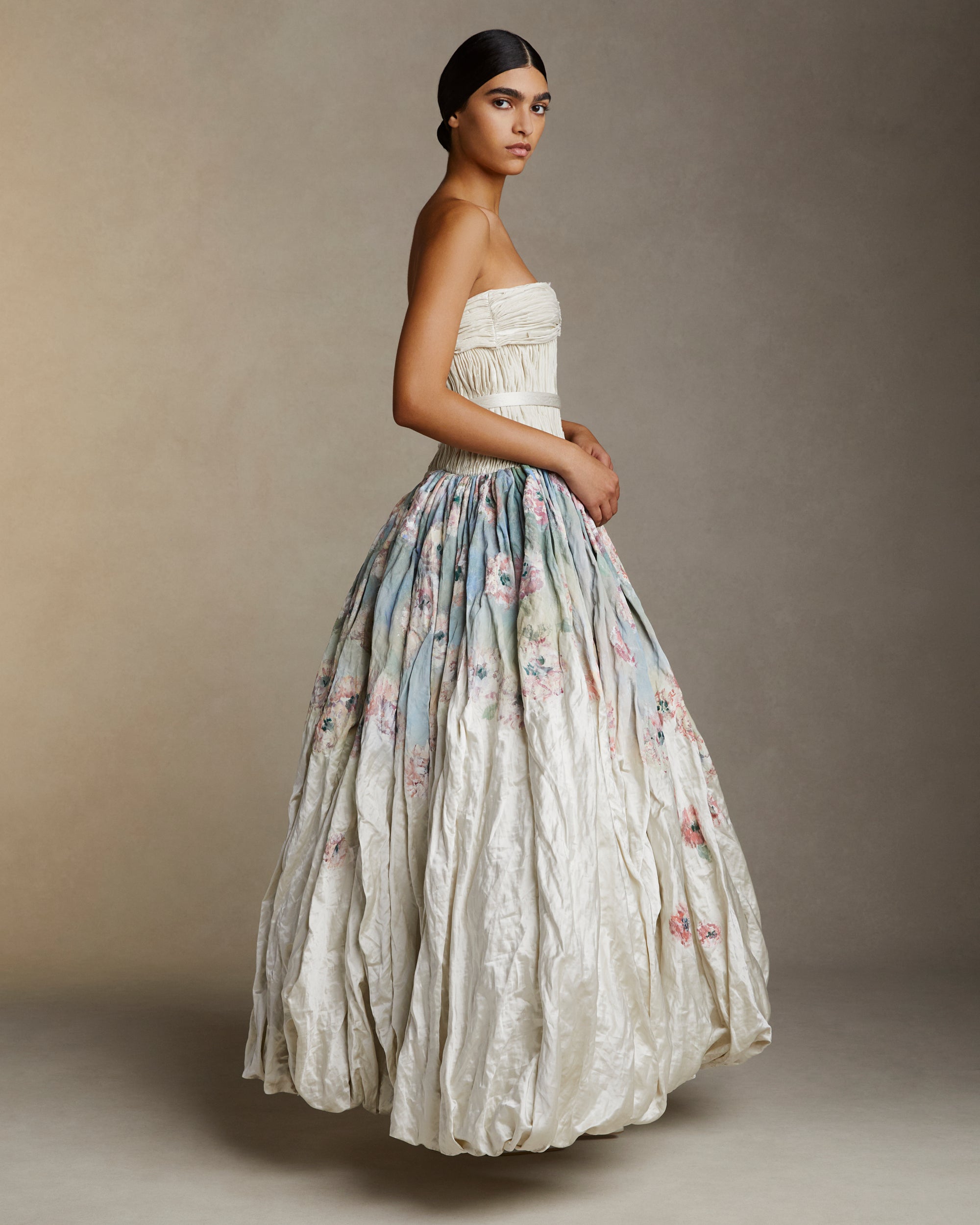 Strapless silk metal gown with hand painted florals that softly degrade down the lightly textured bubble hem skirt. Hand cut bias strip fabric technique decorates the bodice. Invisible zip closure at center back. Sold with self fabric belt. Available without hand painting as well, inquire atelier@daniellefrankelstudio.com for pricing