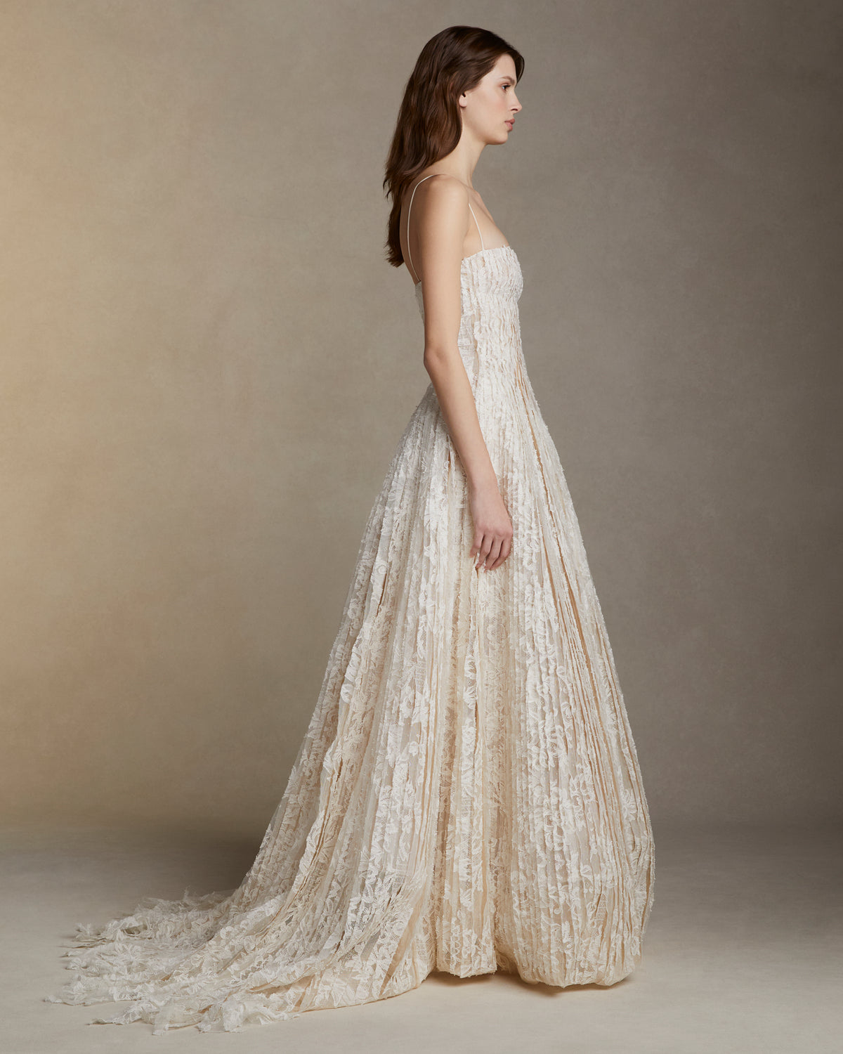 Soft scoop neck ballgown decorated with hand cut Lyon lace strip fabric technique. Layers of Lyon lace strips cascade organically into a released bubble hem train. Internal bustier and invisible zip closure at center back.