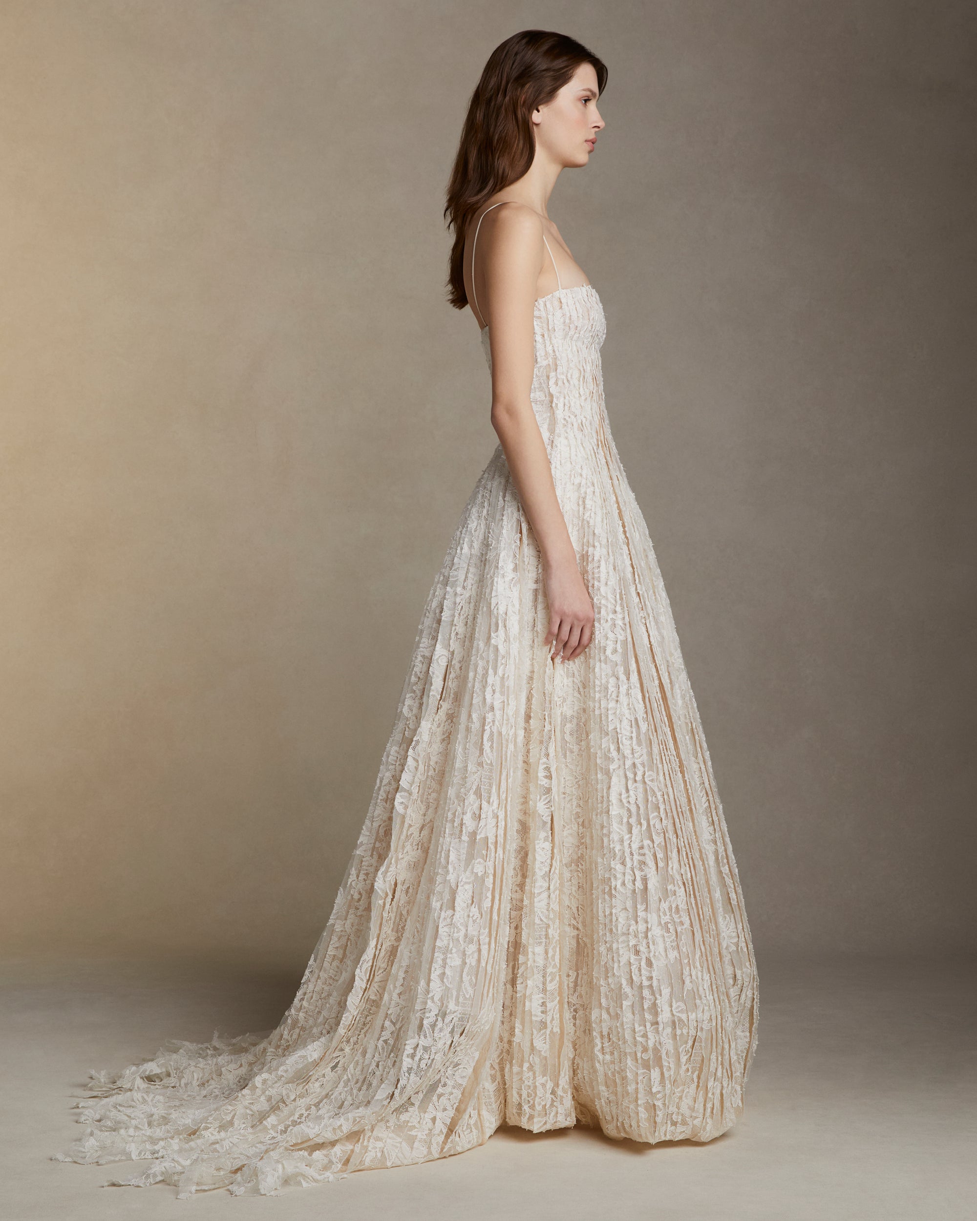 Soft scoop neck ballgown decorated with hand cut Lyon lace strip fabric technique. Layers of Lyon lace strips cascade organically into a released bubble hem train. Internal bustier and invisible zip closure at center back.
