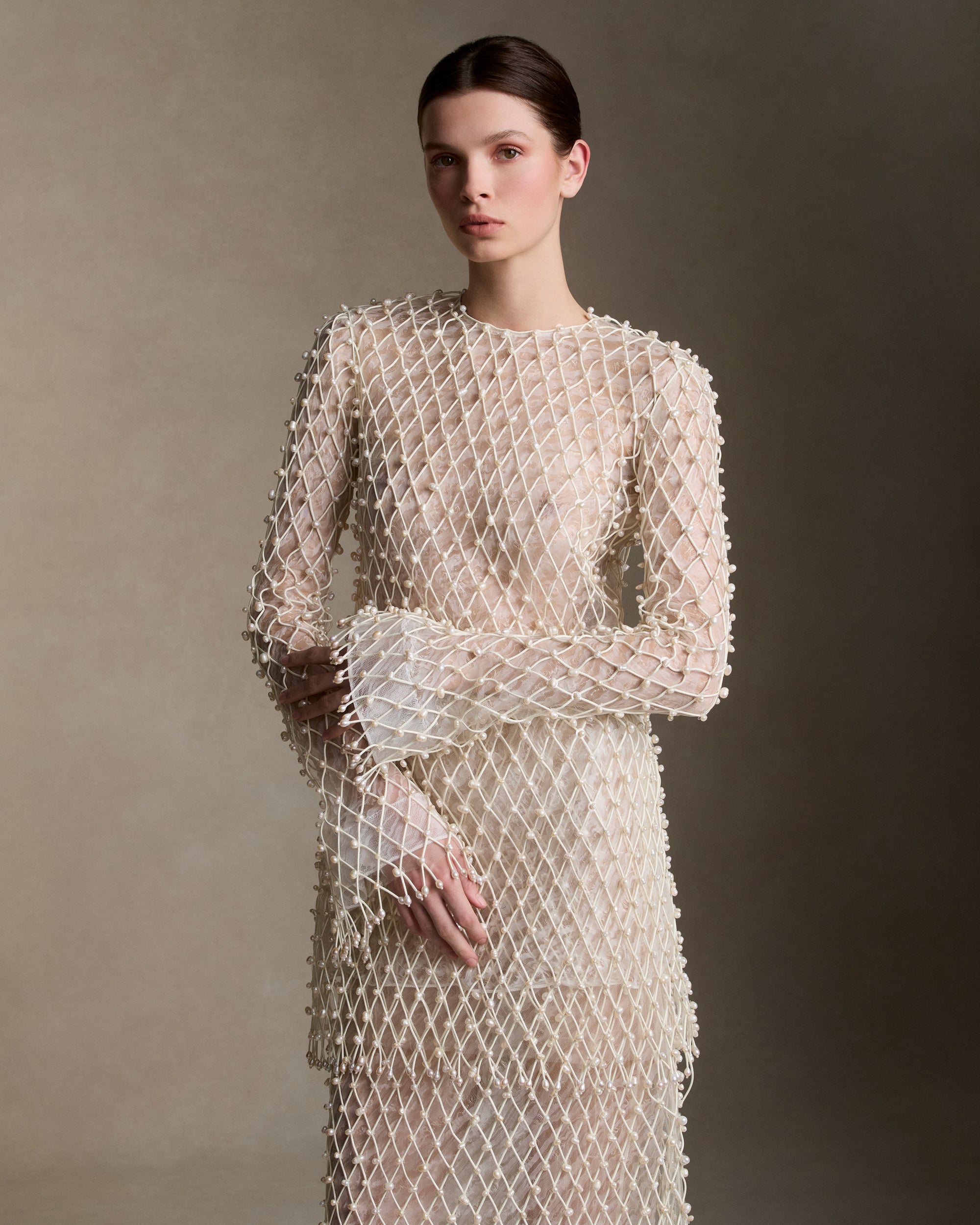 Warped transparent organza mini dress with hand applied corded trellis embroidery embellished in transparent sequins and baroque pearls. Horsehair trim creates a bell sleeve silhouette and fringe hem detailing is finished with genuine teardrop pearls. Bobinette lining with boned internal bustier. Invisible zip and baroque pearl closure at center back.Styled with Blanche skirt