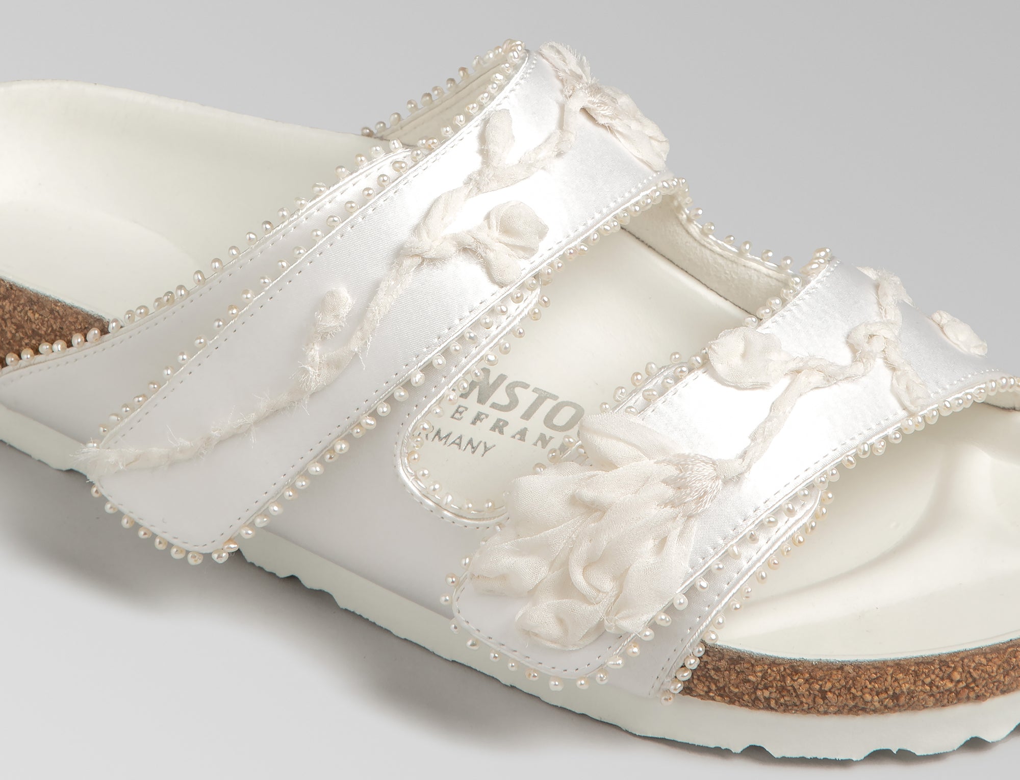 The iconic Arizona is elevated in luminous ivory satin with piped trim detail. Bespoke twisted chiffon embroidered florals and delicate micro pearl edging decorate the straps. The design also introduces an innovative adjustable hidden buckle closure. Hand crafted in Germany. Exclusively available through Danielle Frankel Studio.- Upper: Delicate satin upper, silk trim sewn into folded edges for premium tuxedo like finish- Footbed: Anatomical shaped BIRKENSTOCK cork latex Footbed lined with premium Nappa Leather- Sole: EVA die cut outsole with a custom design, blending classic BIRKENSTOCK bone pattern with delicate leaf inspired detailing 