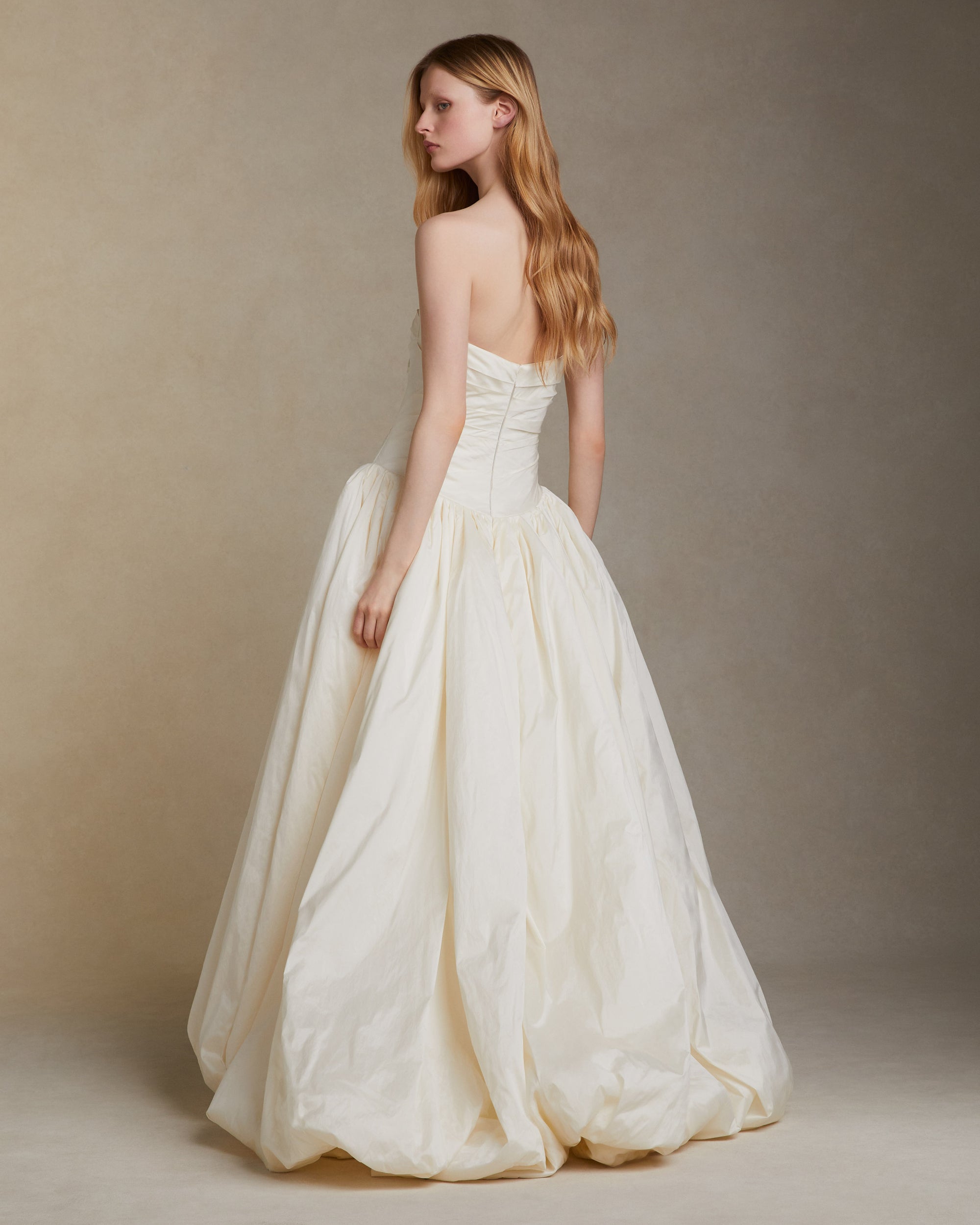 Tissue taffeta draped strapless gown with elongated v waistline. Bubble hem skirt releases from the high hip and peels away from the center front. Invisible zip closure at center back.