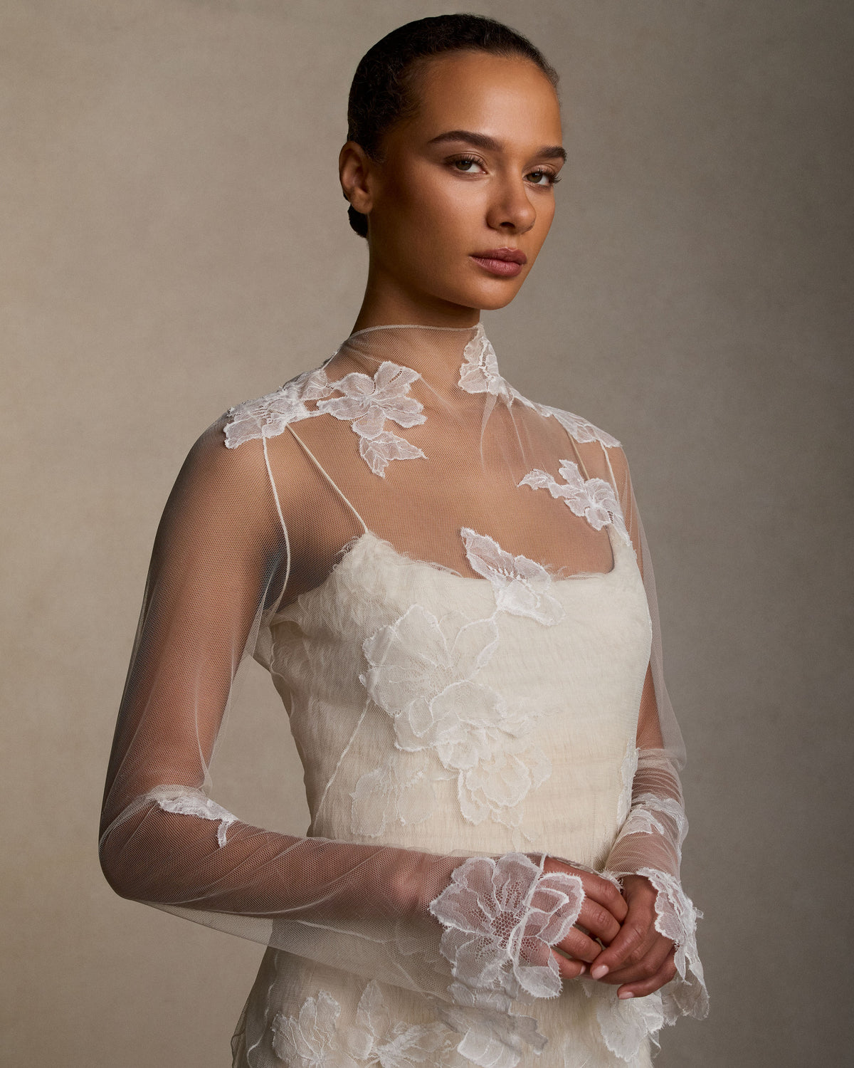Layered hand cut and frayed organza column dress suspended by delicate spaghetti straps. Hand cut corded and chantilly laces emerge from a gradient of ivory organza strips. Left side slit. Boned internal bustier with side zip closure.Styled with Clara Tulle with Lace Appliqué topper