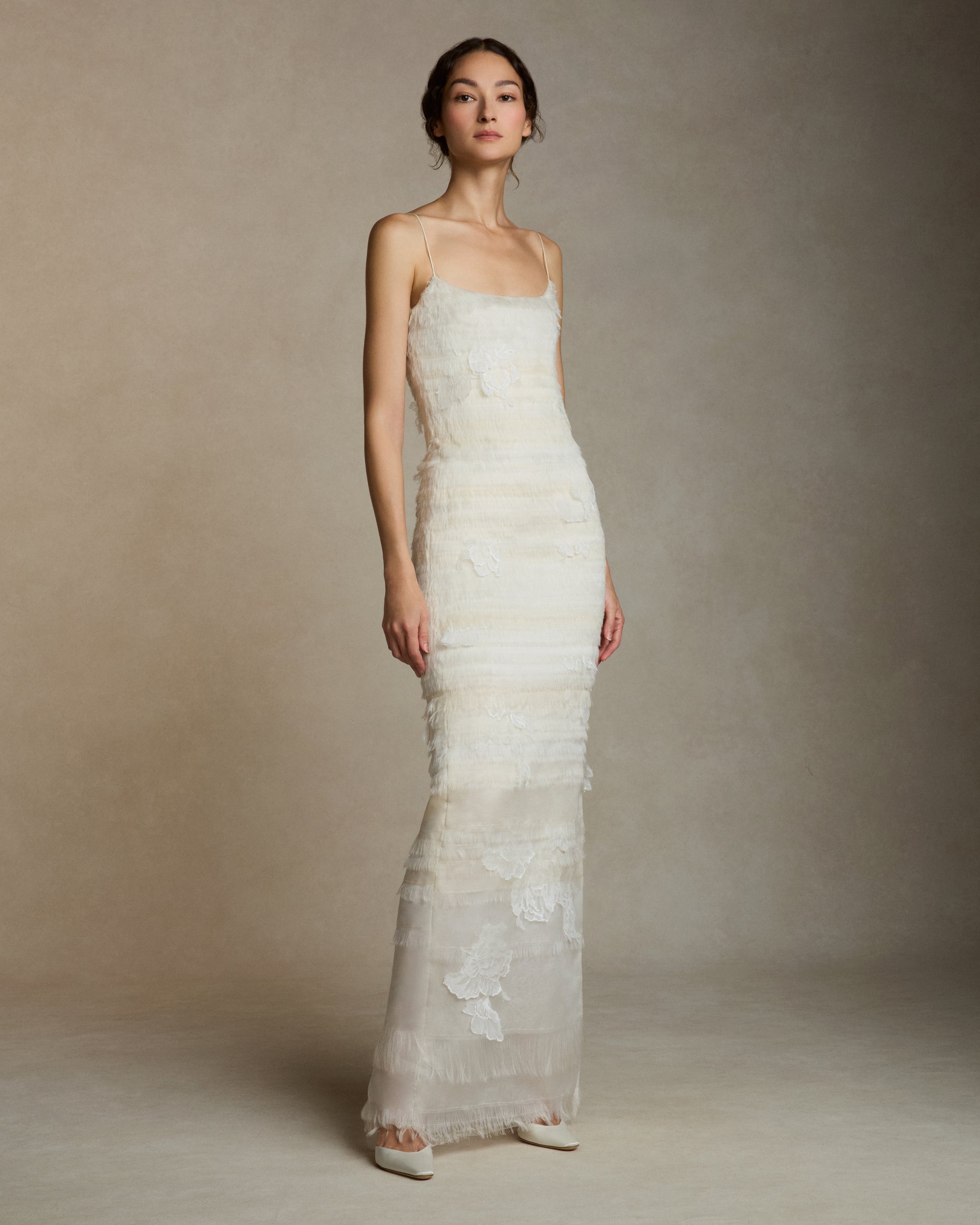 Layered hand cut and frayed organza column dress suspended by delicate spaghetti straps. Hand cut corded and chantilly laces emerge from a gradient of ivory organza strips. Left side slit. Boned internal bustier with side zip closure.Styled with Clara Tulle with Lace Appliqué topper