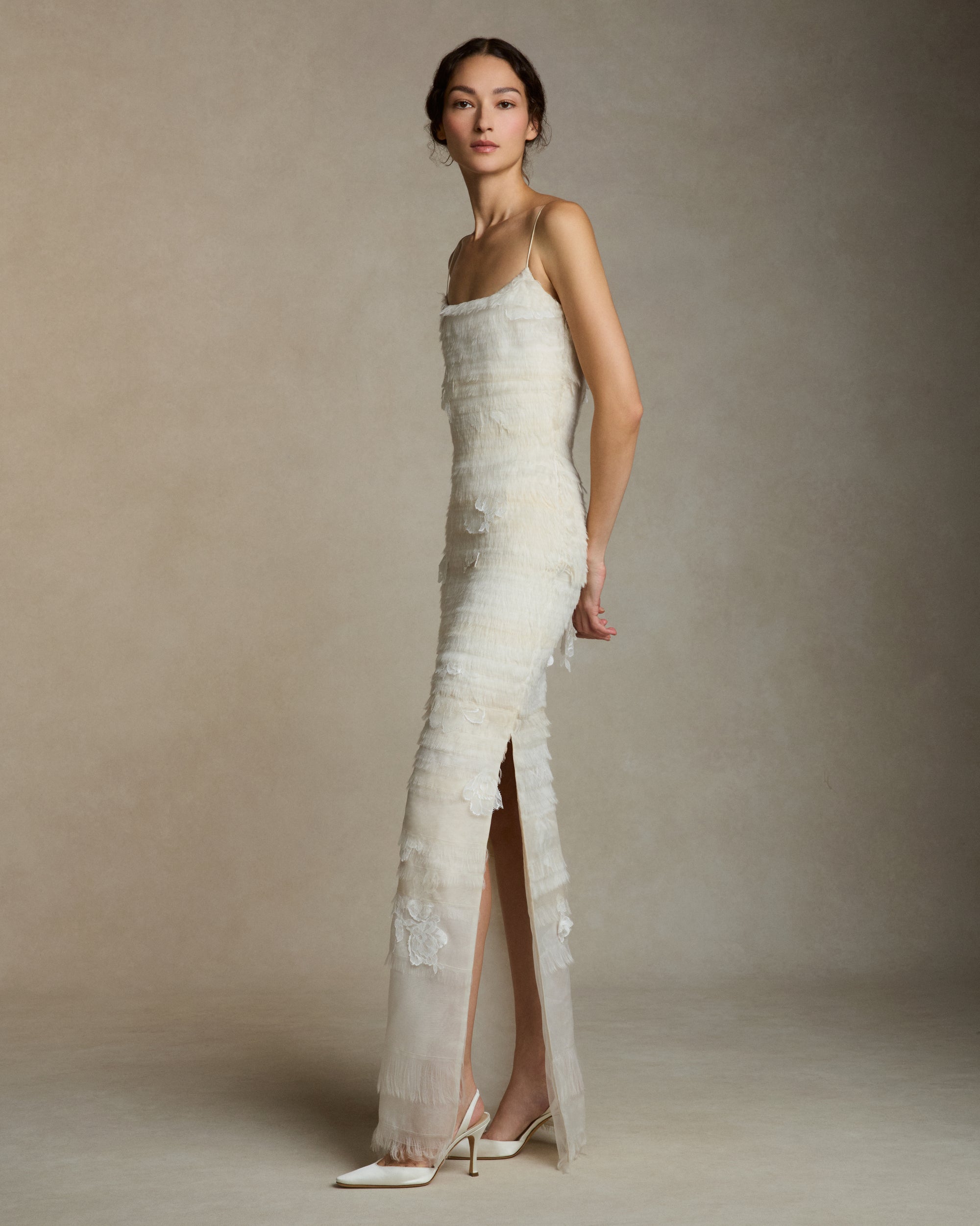 Layered hand cut and frayed organza column dress suspended by delicate spaghetti straps. Hand cut corded and chantilly laces emerge from a gradient of ivory organza strips. Left side slit. Boned internal bustier with side zip closure.Styled with Clara Tulle with Lace Appliqué topper