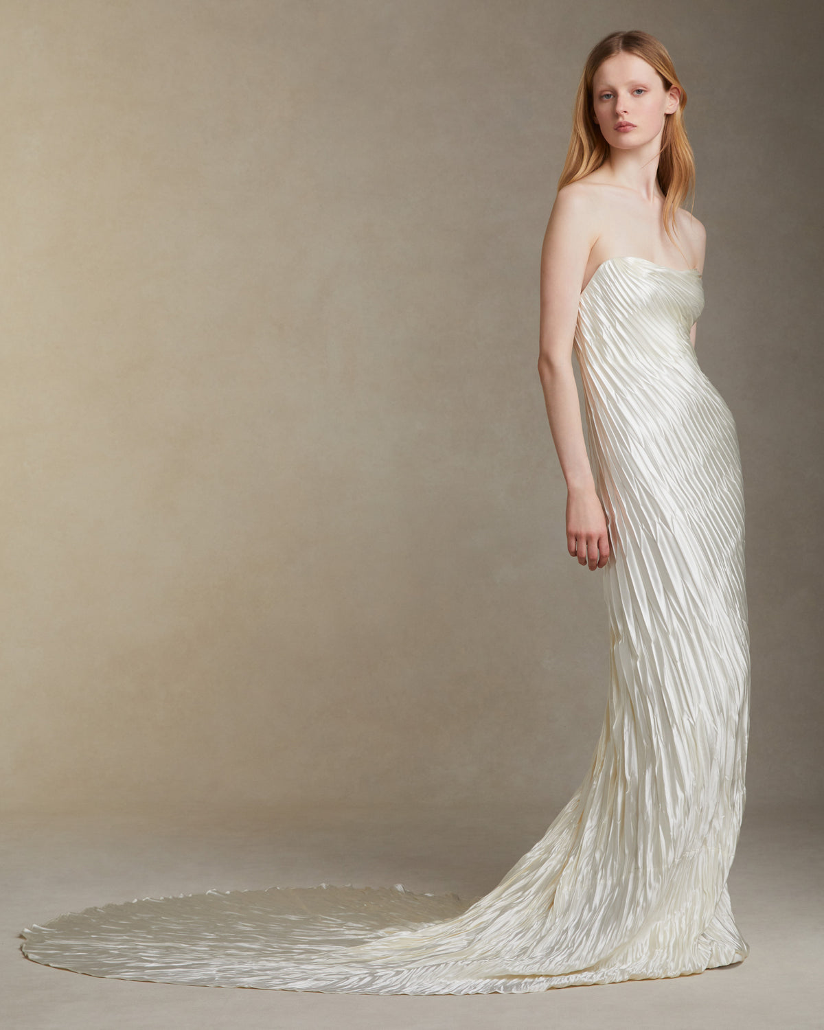 Strapless pleated and hand crinkled silk wool gown with dipped neckline. Fluid draping twists around body and releases into train. Boned internal bustier with soft cups, internal grosgrain waist belt and invisible side zip closure.