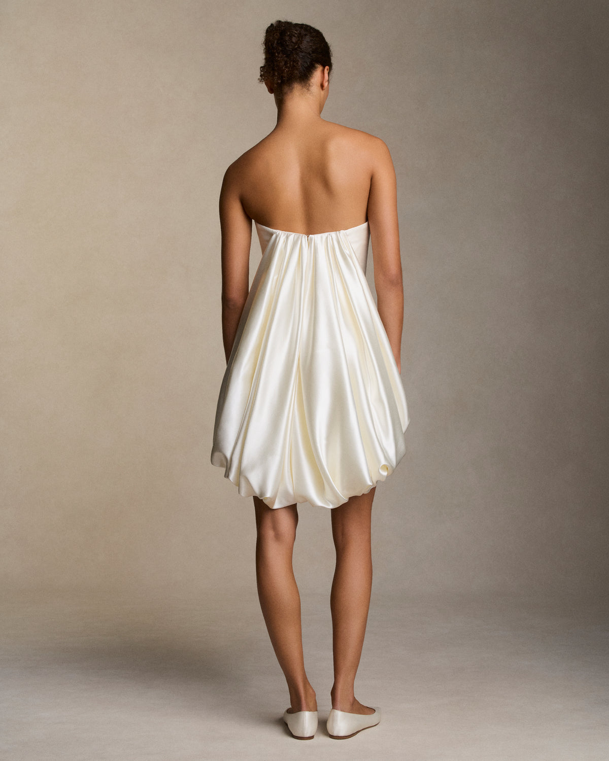 Silk wool twill strapless mini dress with silk wool drape stemming from center front hemline transcending into a fluid draped watteau at center back. Boned internal bustier, internal grosgrain belt and invisible zip closure at center back.