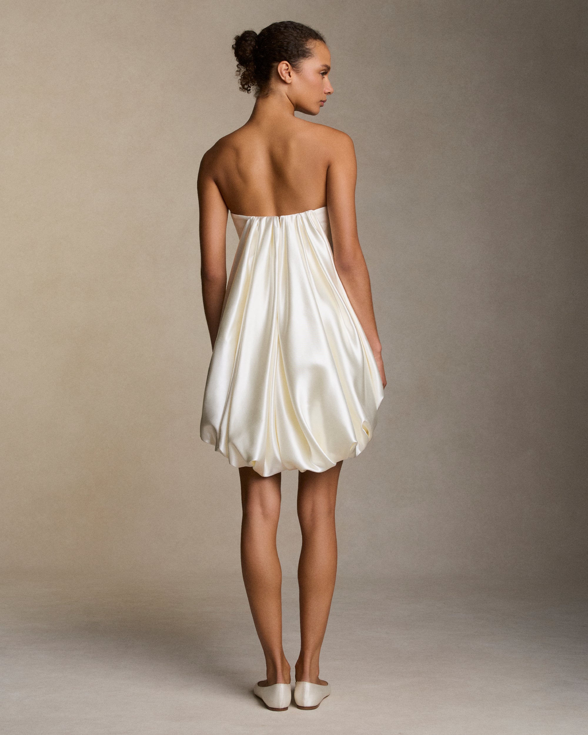 Silk wool twill strapless mini dress with silk wool drape stemming from center front hemline transcending into a fluid draped watteau at center back. Boned internal bustier, internal grosgrain belt and invisible zip closure at center back.