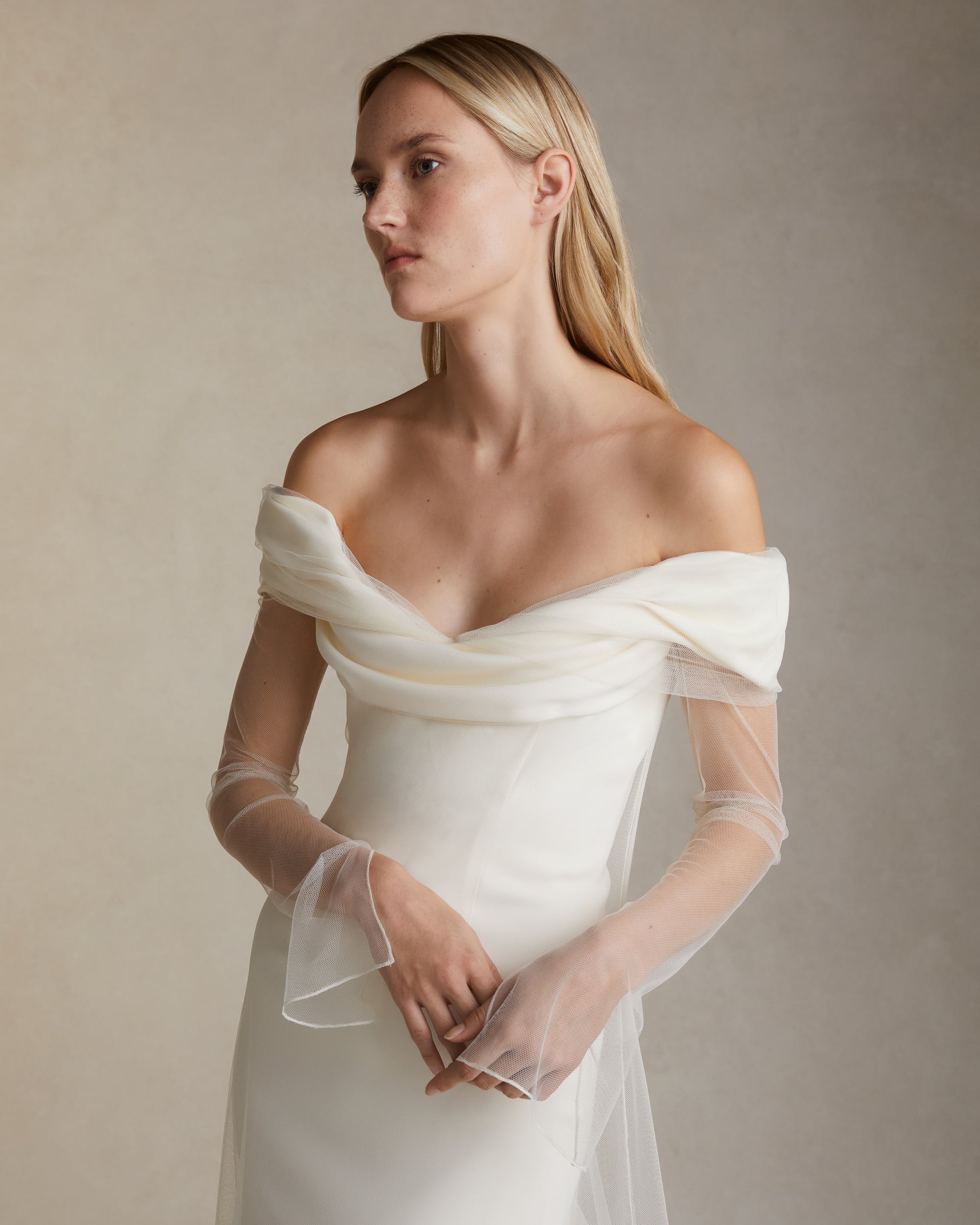 Stretch cady off the shoulder gown with draped bodice detail. Soft tulle overlay extends from neckline. Invisible zip closure at center back.