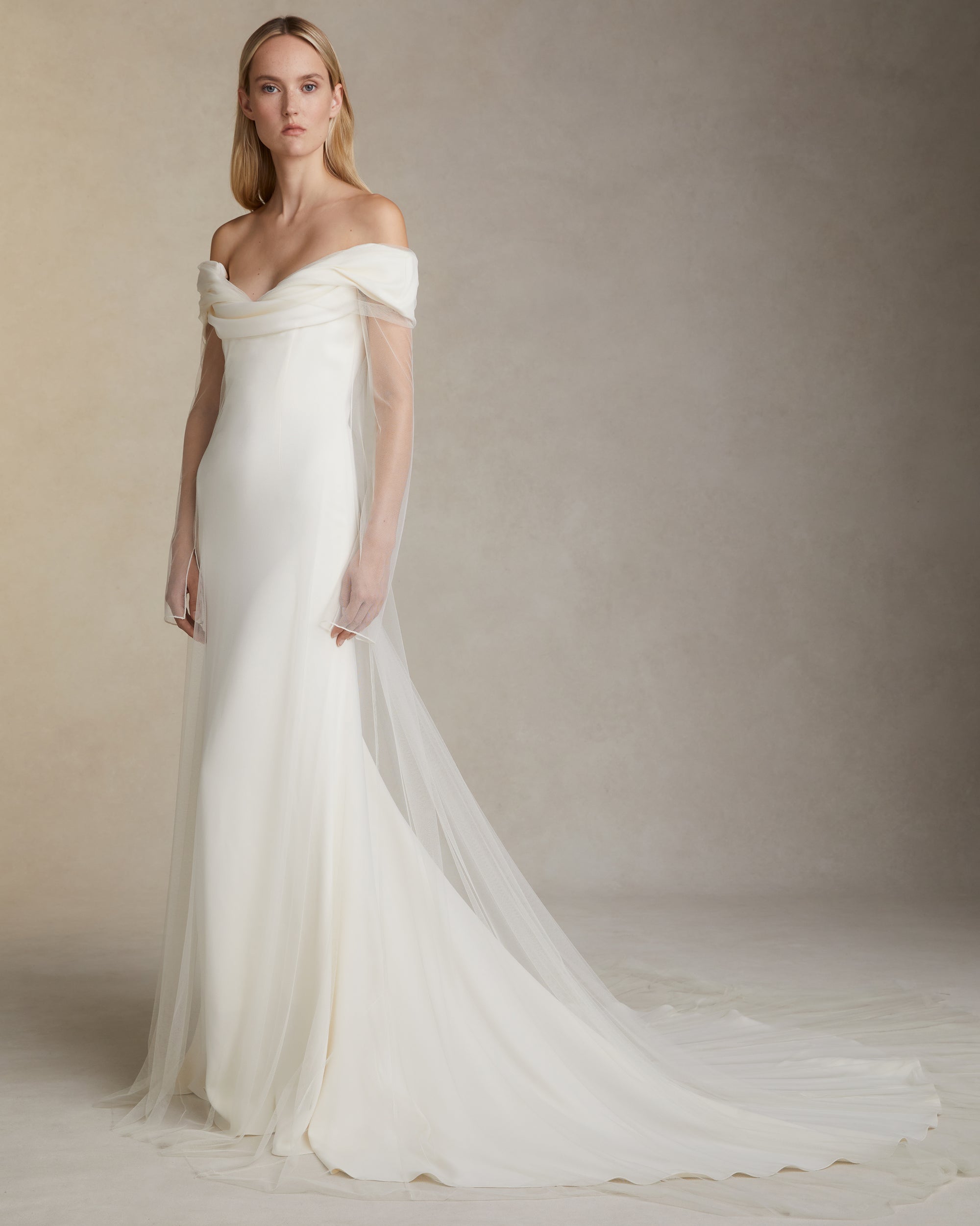 Stretch cady off the shoulder gown with draped bodice detail. Soft tulle overlay extends from neckline. Invisible zip closure at center back.