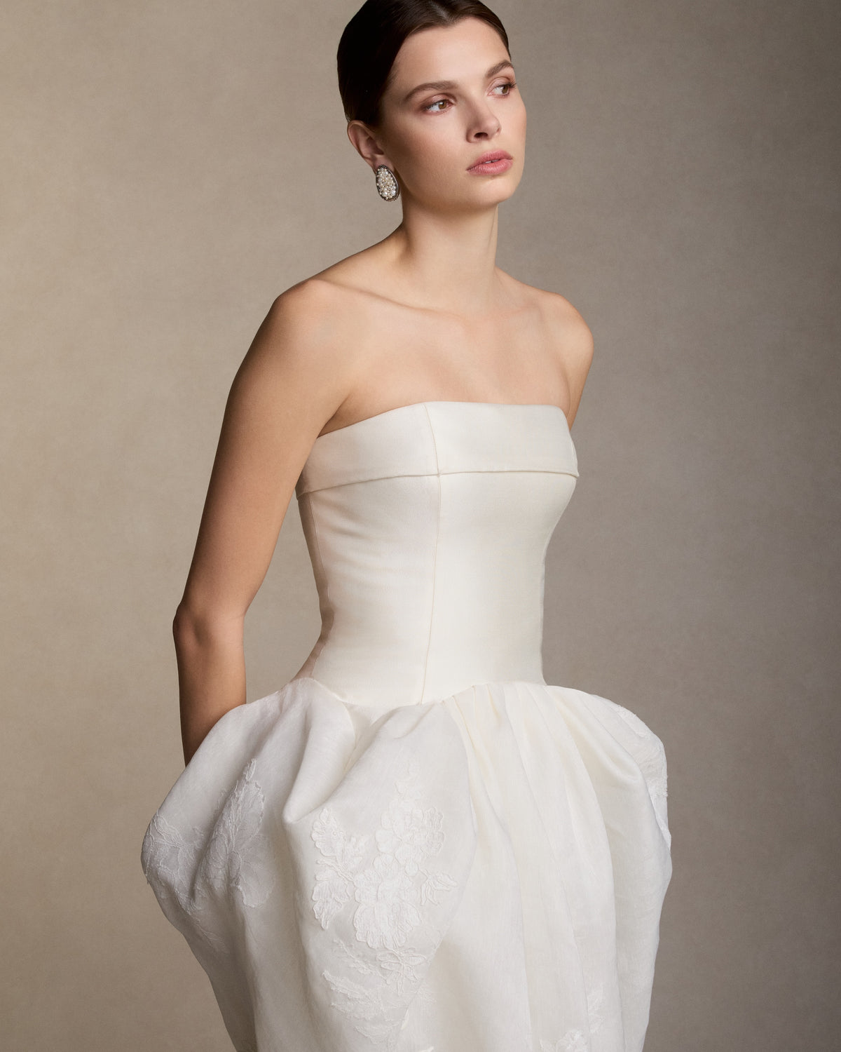 Silk wool twill and linen organza strapless ball gown. Structured silk wool twill bodice is finished with a foldover neckline. A draped linen organza skirt, decorated with hand painted florals and corded and Chantilly lace appliqués, releases into a godet train. Boned internal bustier, internal grosgrain belt and invisible zip closure at center back.
