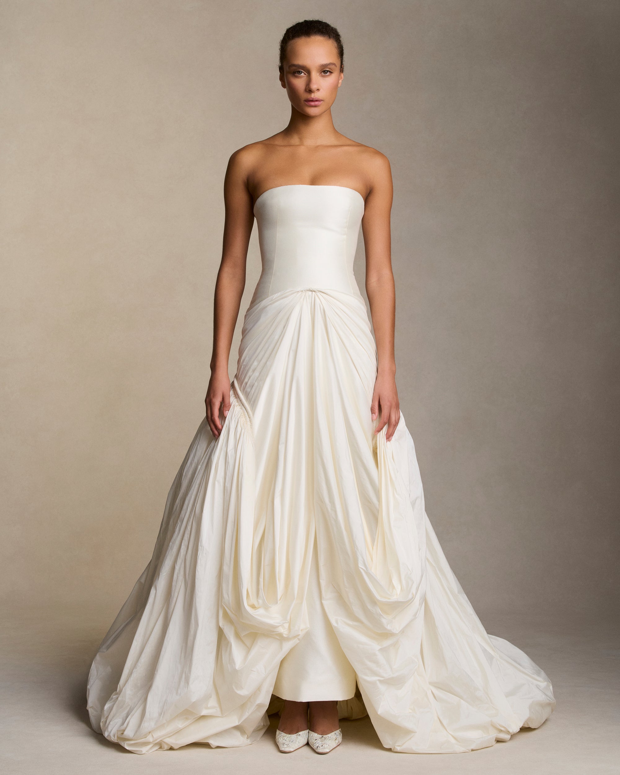 Strapless silk wool twill column gown with draped and gathered tissue taffeta bubble hem skirt. Corded channel detail frames the hip silhouette disappearing into draped pickup detail at center front. Boned internal bustier, internal grosgrain belt and invisible zip closure at center back.