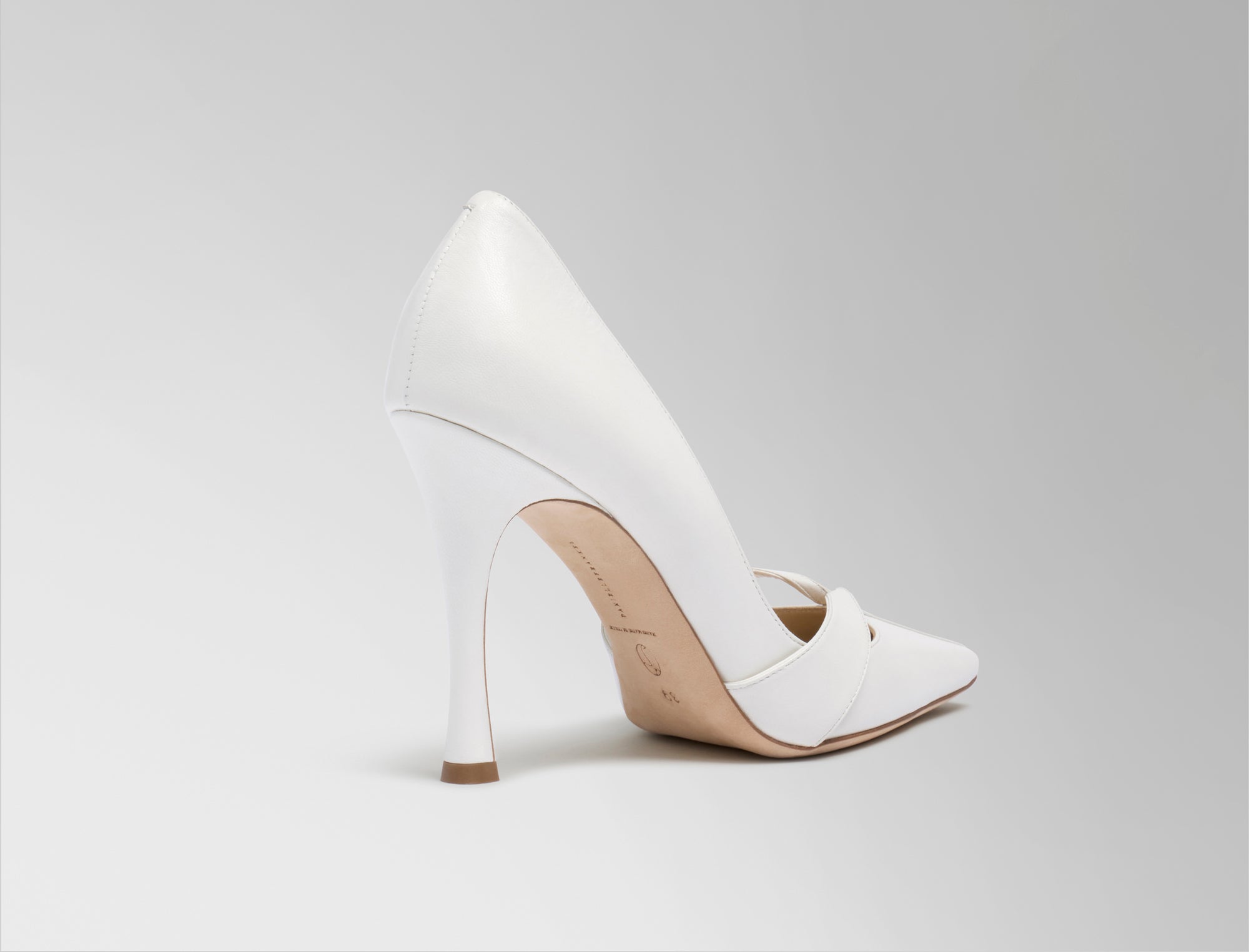 Rounded square toe pump crafted in Italy of ivory leather. Leather trim detail decorates the toe, peeling away at neckline as it wraps around the foot. 100mm heel.