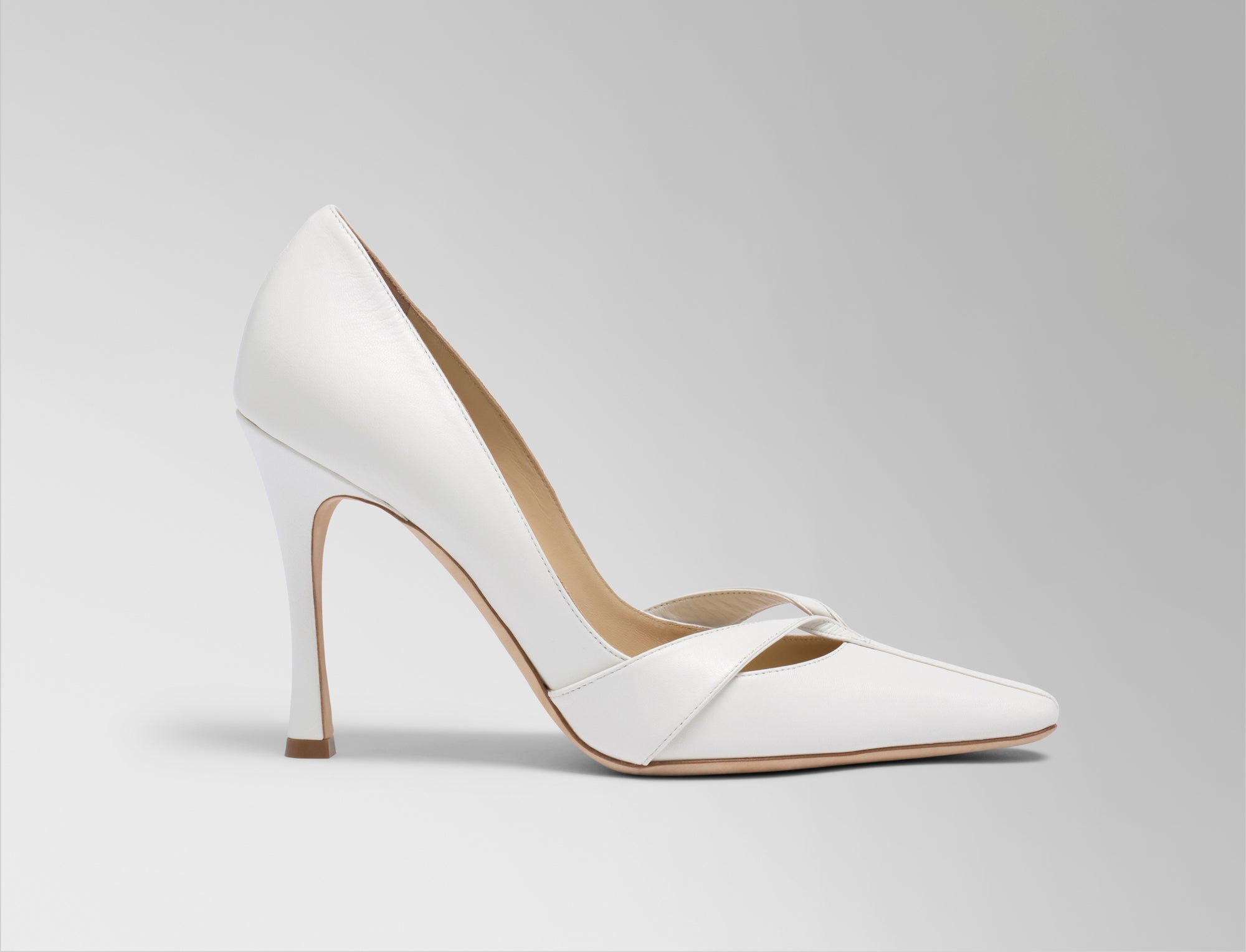 Rounded square toe pump crafted in Italy of ivory leather. Leather trim detail decorates the toe, peeling away at neckline as it wraps around the foot. 100mm heel.