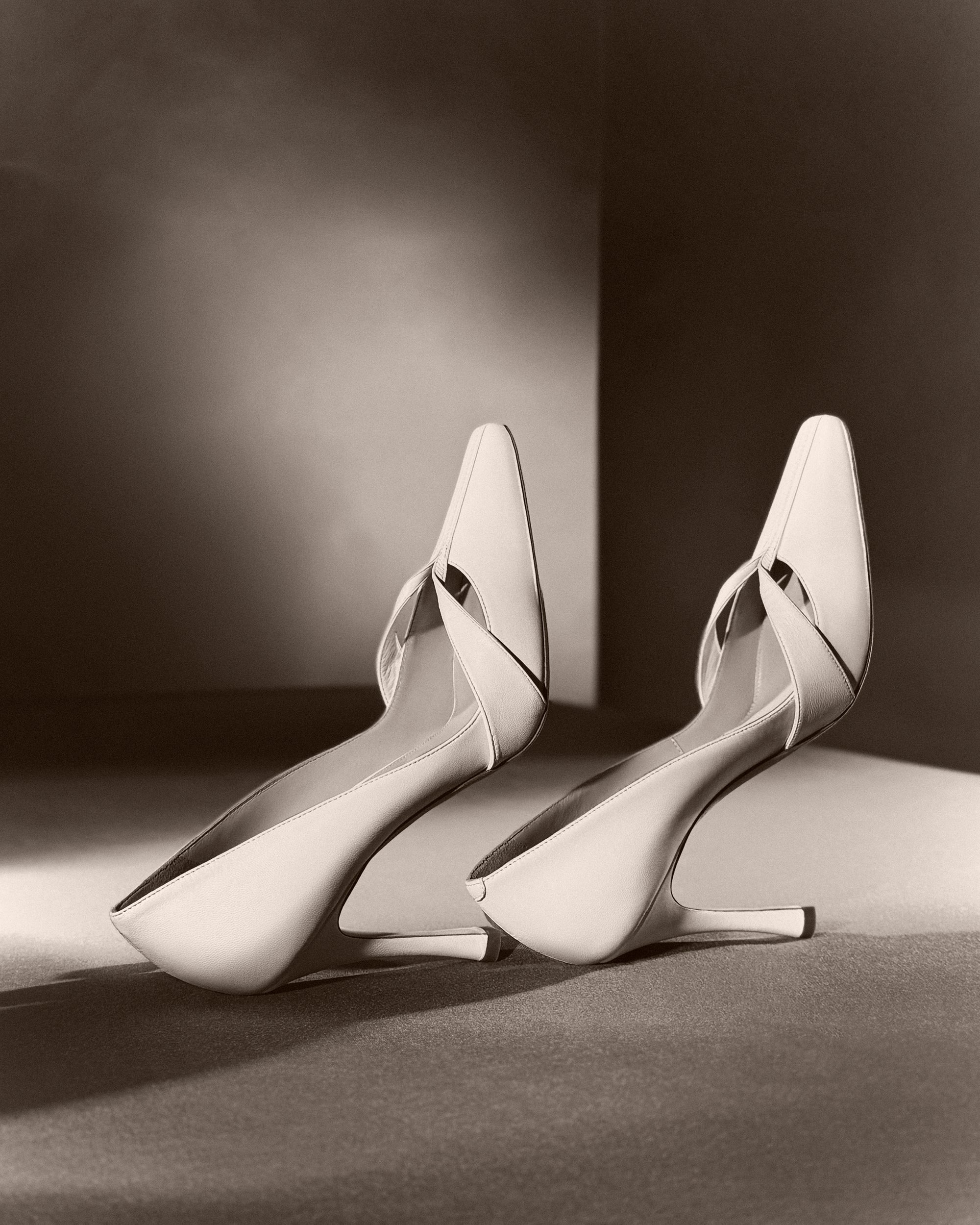 Rounded square toe pump crafted in Italy of ivory leather. Leather trim detail decorates the toe, peeling away at neckline as it wraps around the foot. 100mm heel.