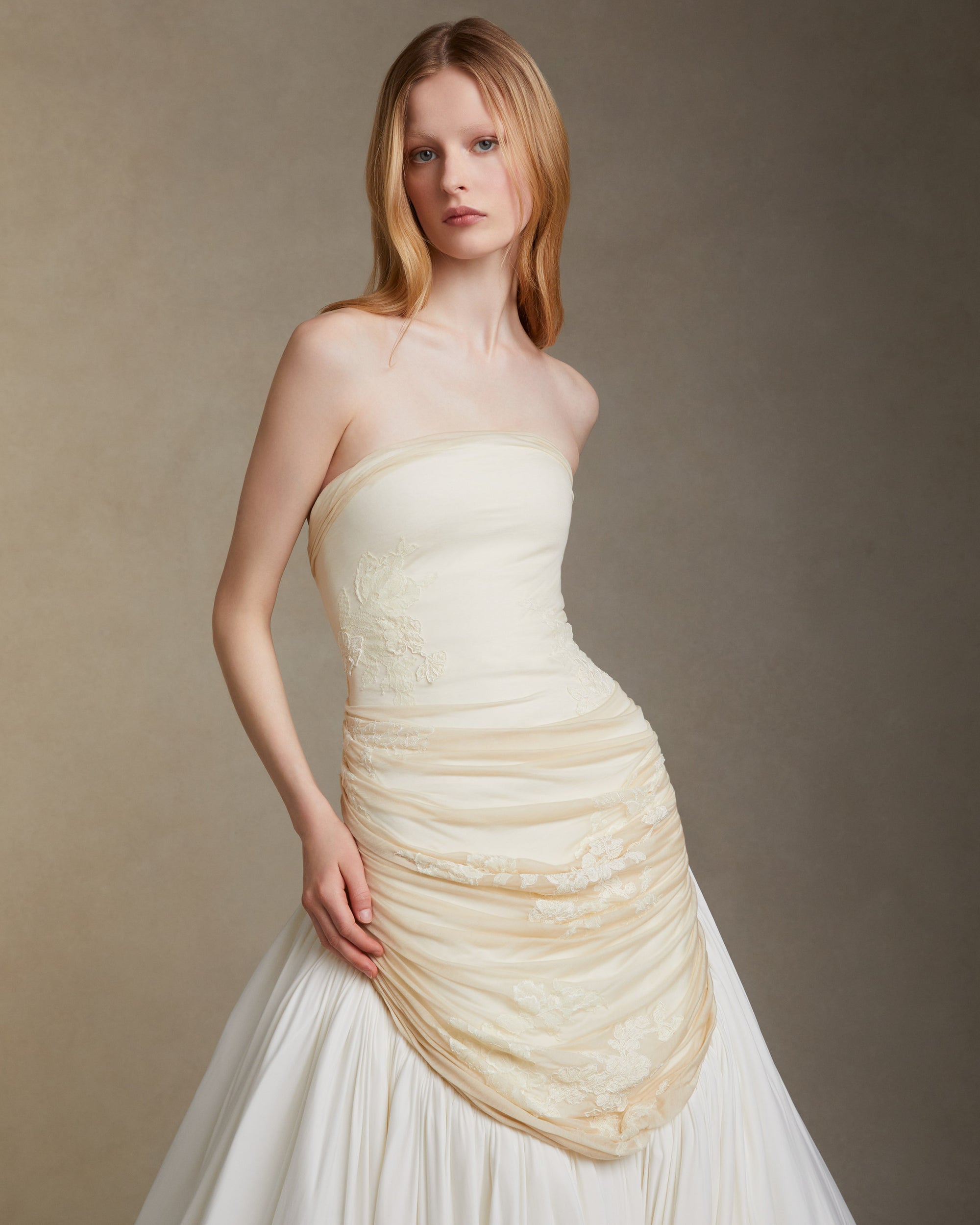 Fluid jersey strapless gown with asymmetric waistline that dips into a bubbled hem with train. Elongated bodice is draped with silk jersey and decorated in hand cut and corded chantilly lace appliques. Invisible zip closure at center back.