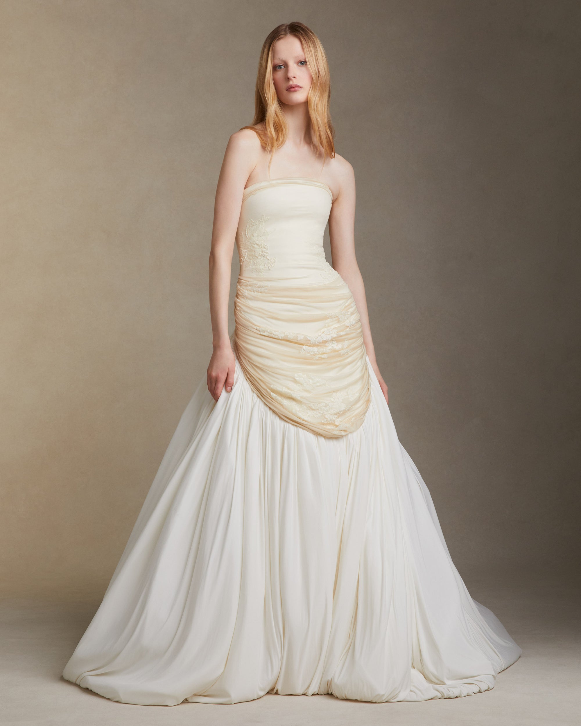 Fluid jersey strapless gown with asymmetric waistline that dips into a bubbled hem with train. Elongated bodice is draped with silk jersey and decorated in hand cut and corded chantilly lace appliques. Invisible zip closure at center back.