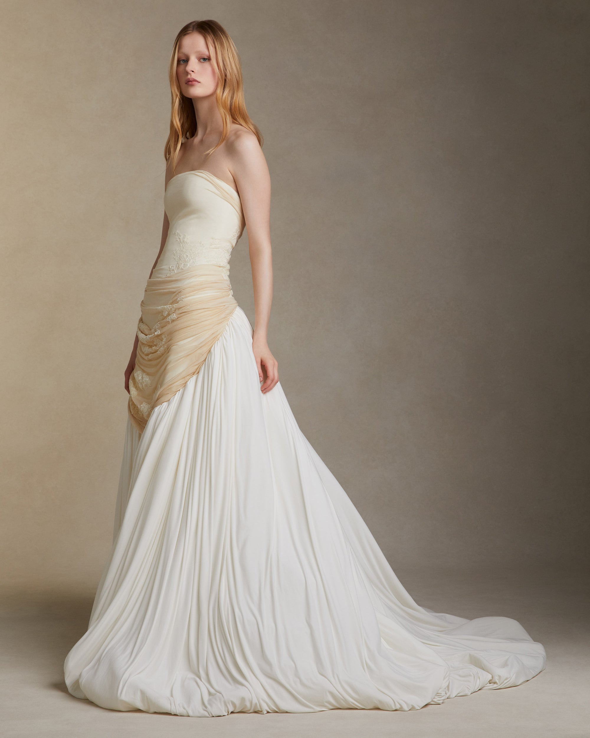 Fluid jersey strapless gown with asymmetric waistline that dips into a bubbled hem with train. Elongated bodice is draped with silk jersey and decorated in hand cut and corded chantilly lace appliques. Invisible zip closure at center back.
