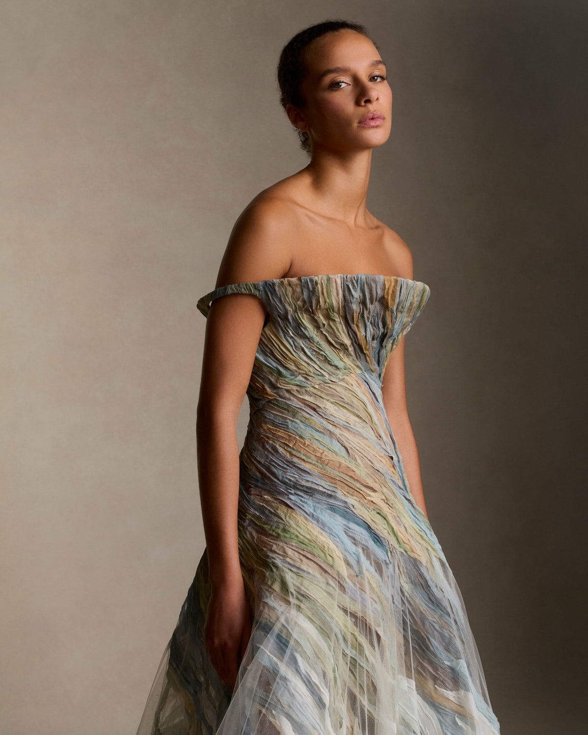 Strapless illusion tulle gown with sculptural flared neckline. Hand dyed hand cut silk chiffon watercolor strips ripple around the body, cascading into a bubble hem. Boned internal bustier, internal grosgrain belt and invisible zip closure at center back.