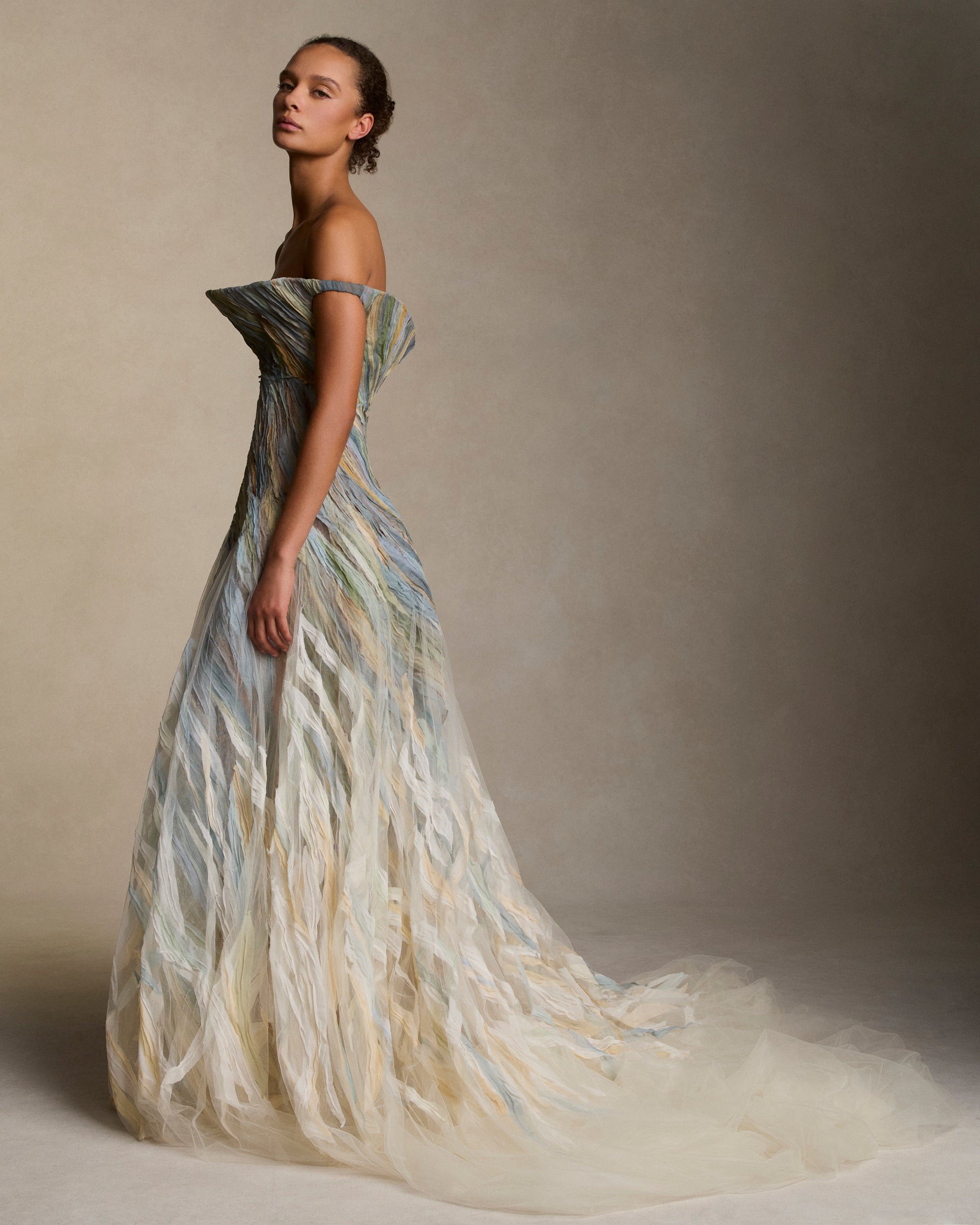 Strapless illusion tulle gown with sculptural flared neckline. Hand dyed hand cut silk chiffon watercolor strips ripple around the body, cascading into a bubble hem. Boned internal bustier, internal grosgrain belt and invisible zip closure at center back.