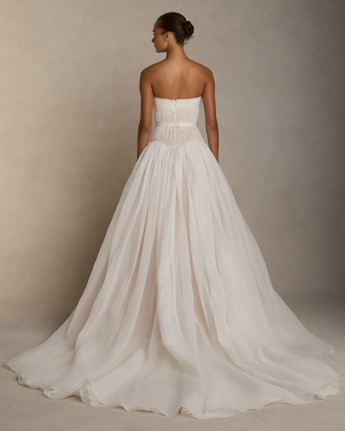 Strapless crinkle organza gown with soft ball skirt. Crinkle organza bias strip embroidery decorates the bodice, veiling a nude bobinette bustier. Invisible zip closure at center back. Sold with a self fabric belt.