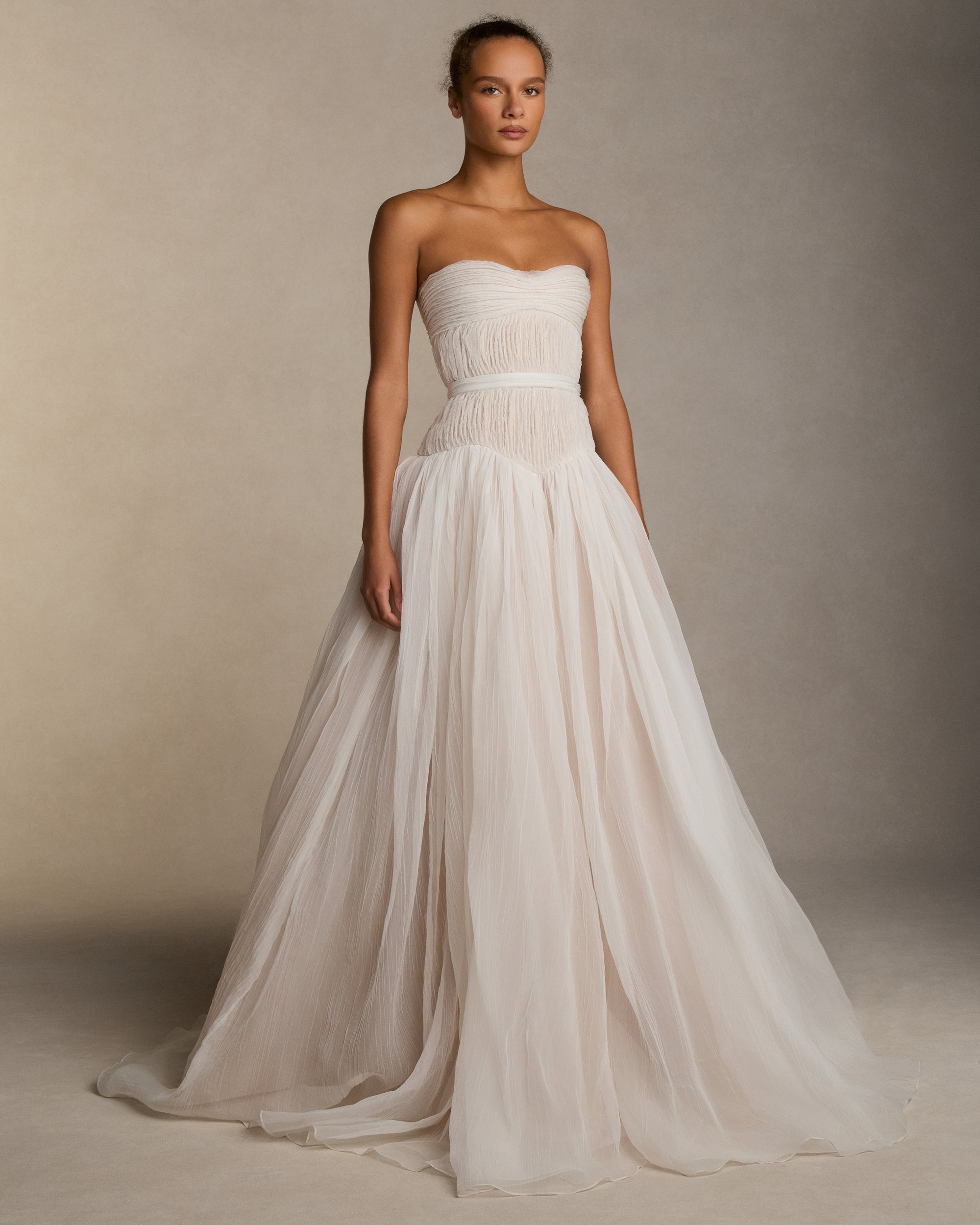 Strapless crinkle organza gown with soft ball skirt. Crinkle organza bias strip embroidery decorates the bodice, veiling a nude bobinette bustier. Invisible zip closure at center back. Sold with a self fabric belt.
