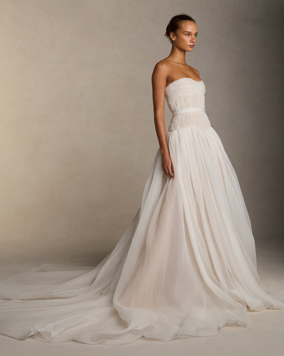 Strapless crinkle organza gown with soft ball skirt. Crinkle organza bias strip embroidery decorates the bodice, veiling a nude bobinette bustier. Invisible zip closure at center back. Sold with a self fabric belt.