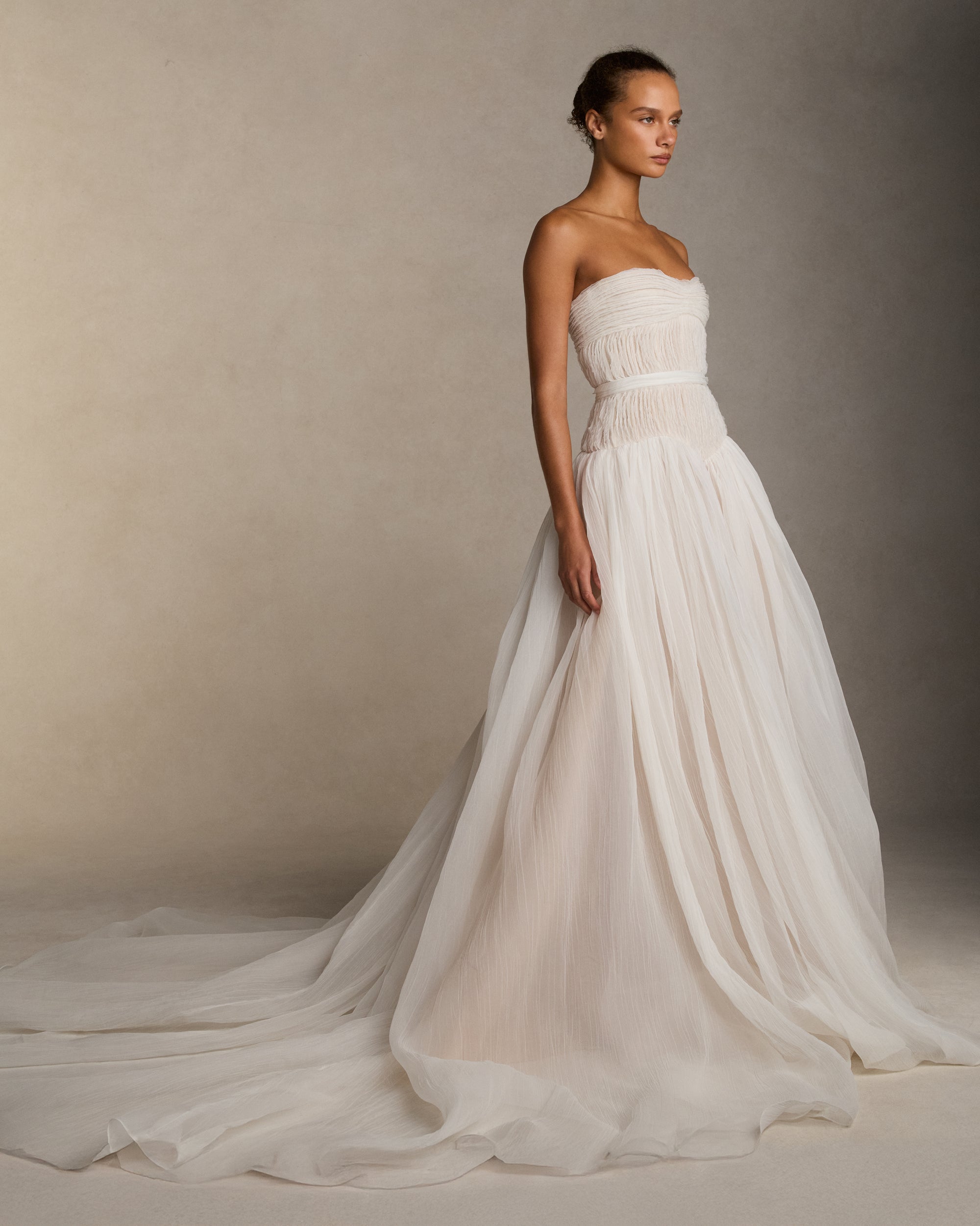 Strapless crinkle organza gown with soft ball skirt. Crinkle organza bias strip embroidery decorates the bodice, veiling a nude bobinette bustier. Invisible zip closure at center back. Sold with a self fabric belt.
