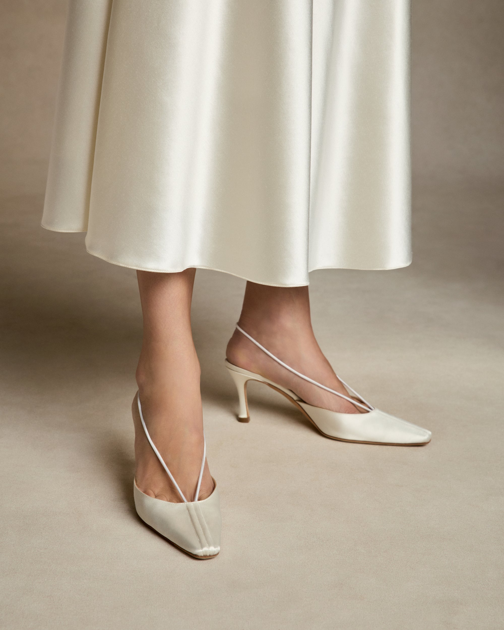 70mm rounded square toe mule crafted in Italy of ivory satin. Elastic sling back wraps around the foot, finishing into a channel detail at toe.