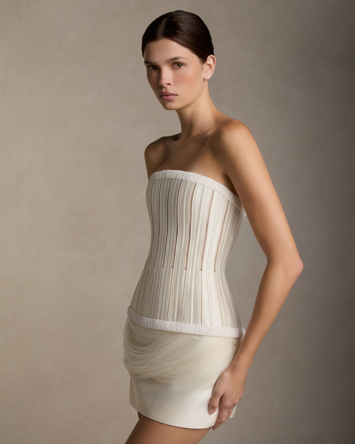 Silk wool twill mini skirt with boned yoke detail. Tulle draping wraps around the waist twisting into an asymmetric train at back. Invisible zip closure at center back.Styled with Ivy bustier