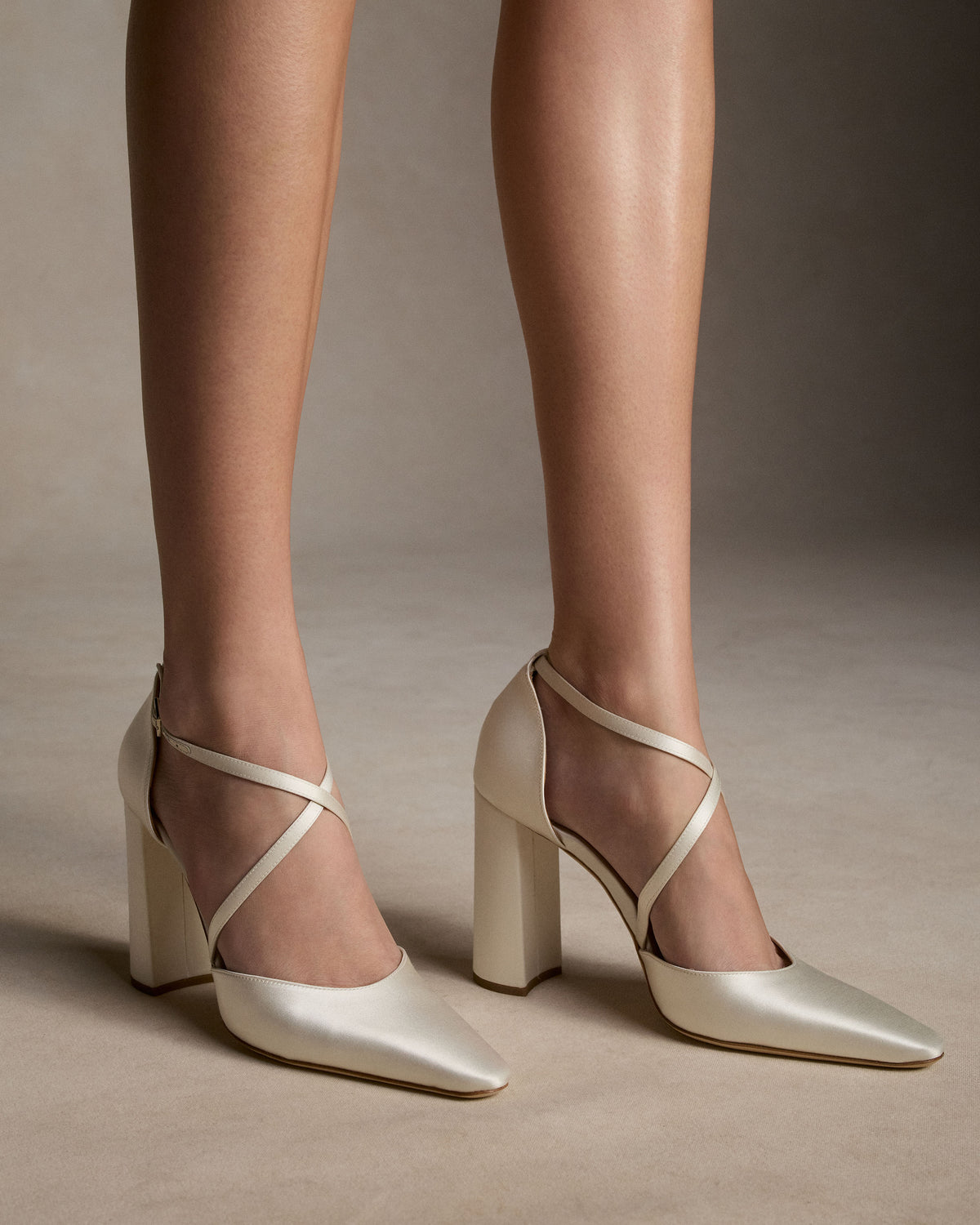 Classic rounded square toe pump with criss cross ankle strap, crafted in Italy of ivory satin. 100mm block heel.